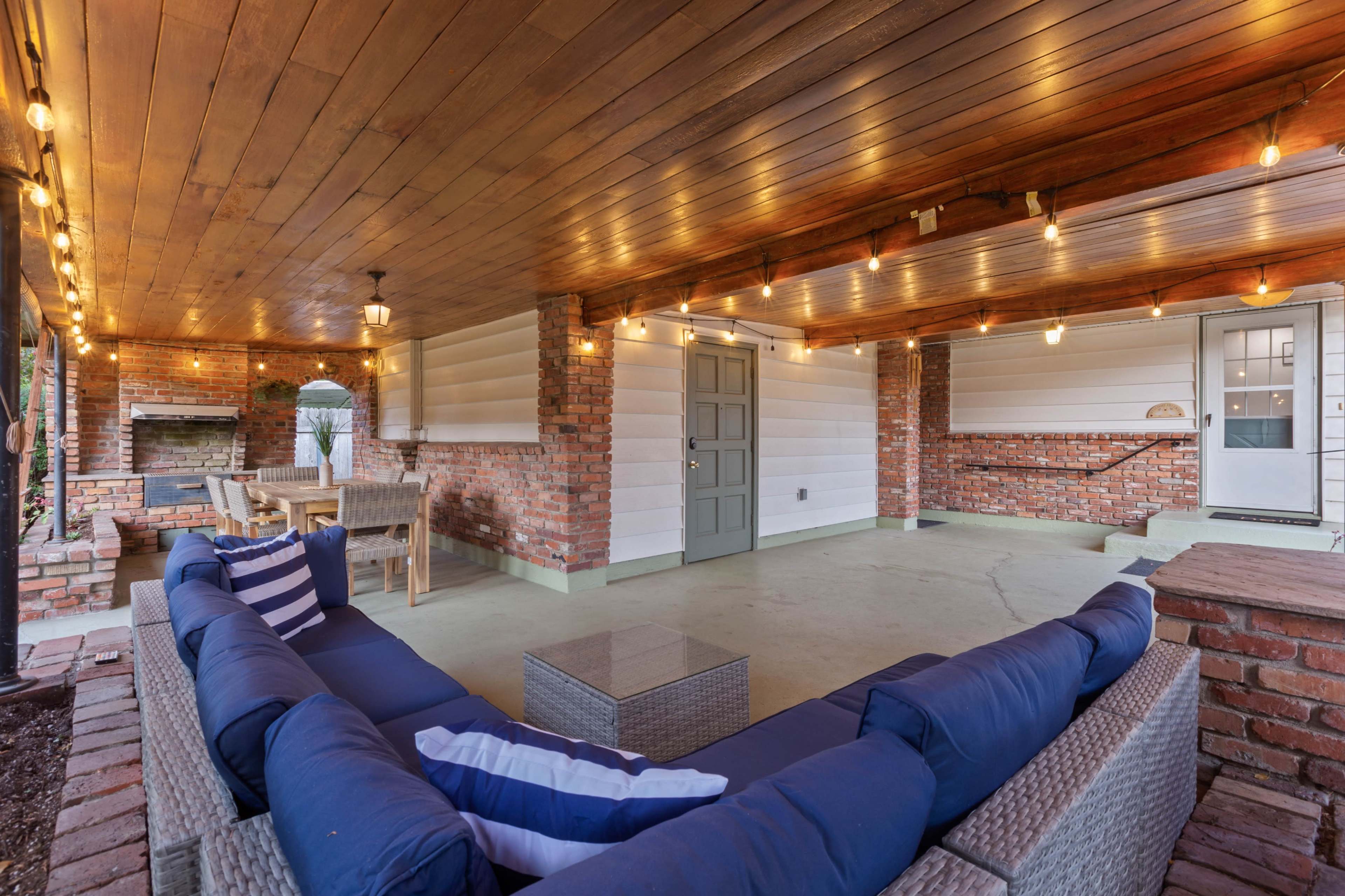 A covered outdoor patio with a seating area, dining space, and string lights overhead.