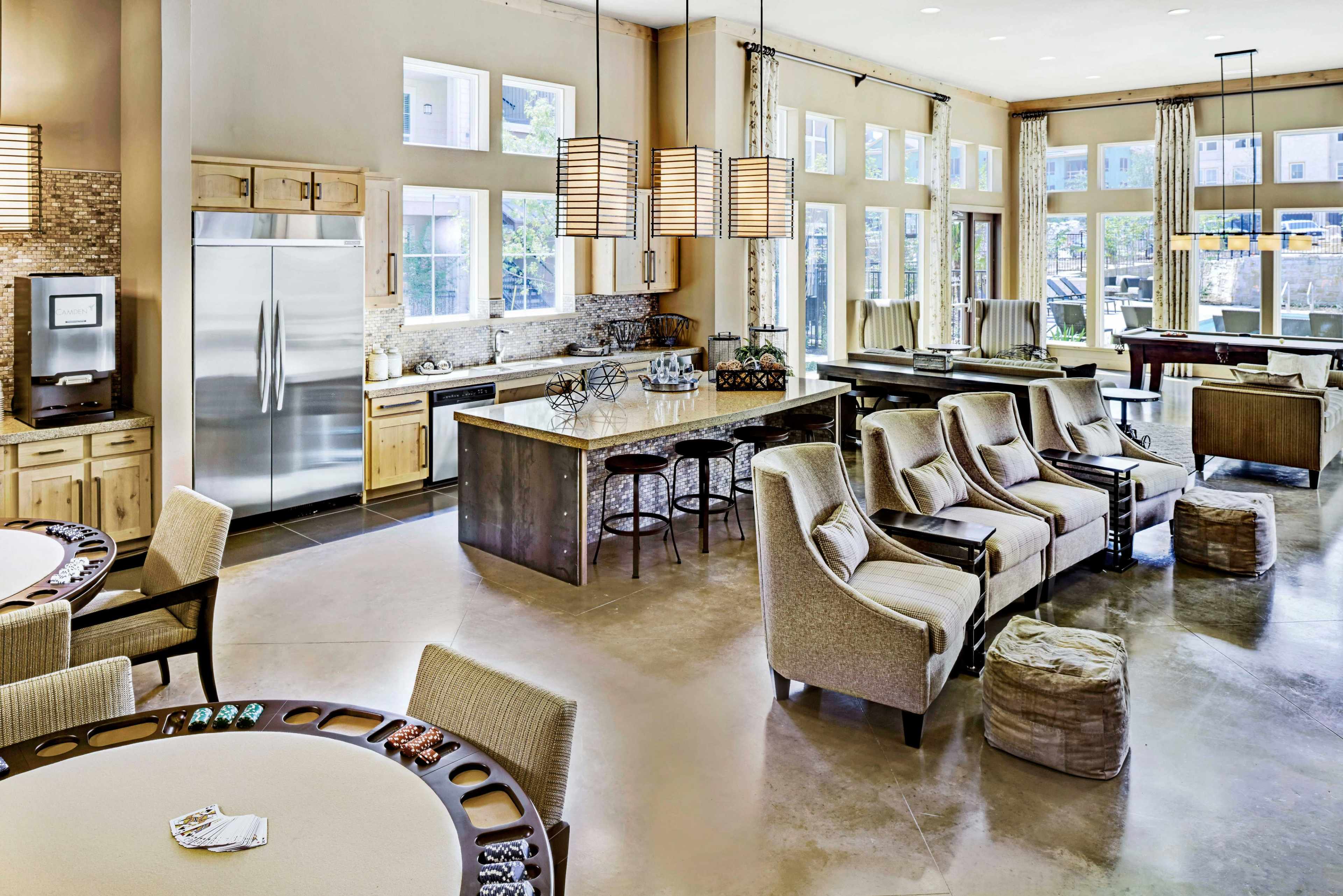 A spacious, modern common area with a kitchen, dining space, and seating arrangements featuring large windows that let in natural light.