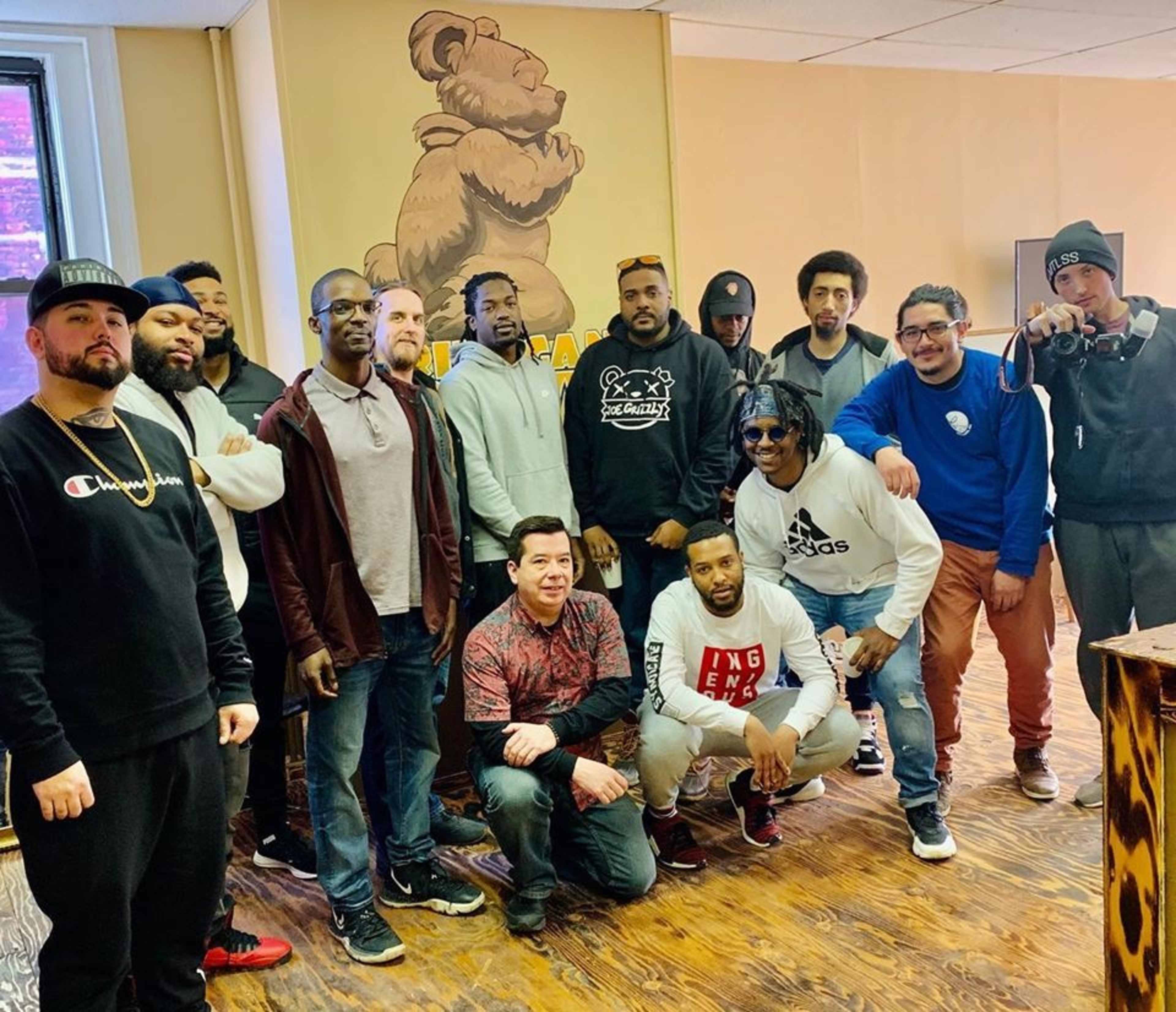 A group of men poses together in a room featuring a large bear mural on the wall.