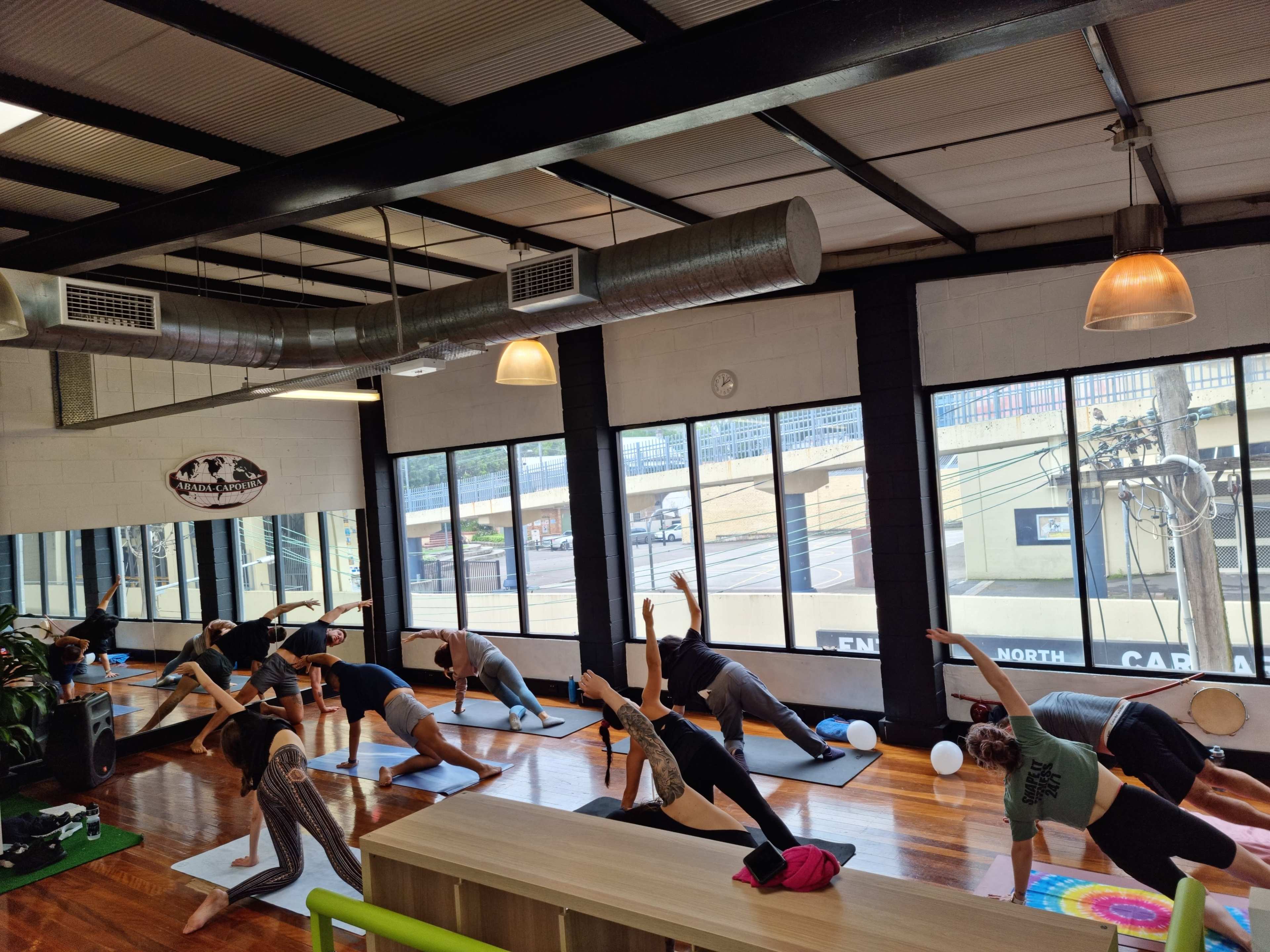 A group of people are practicing yoga in a spacious studio with large windows and wooden floors.