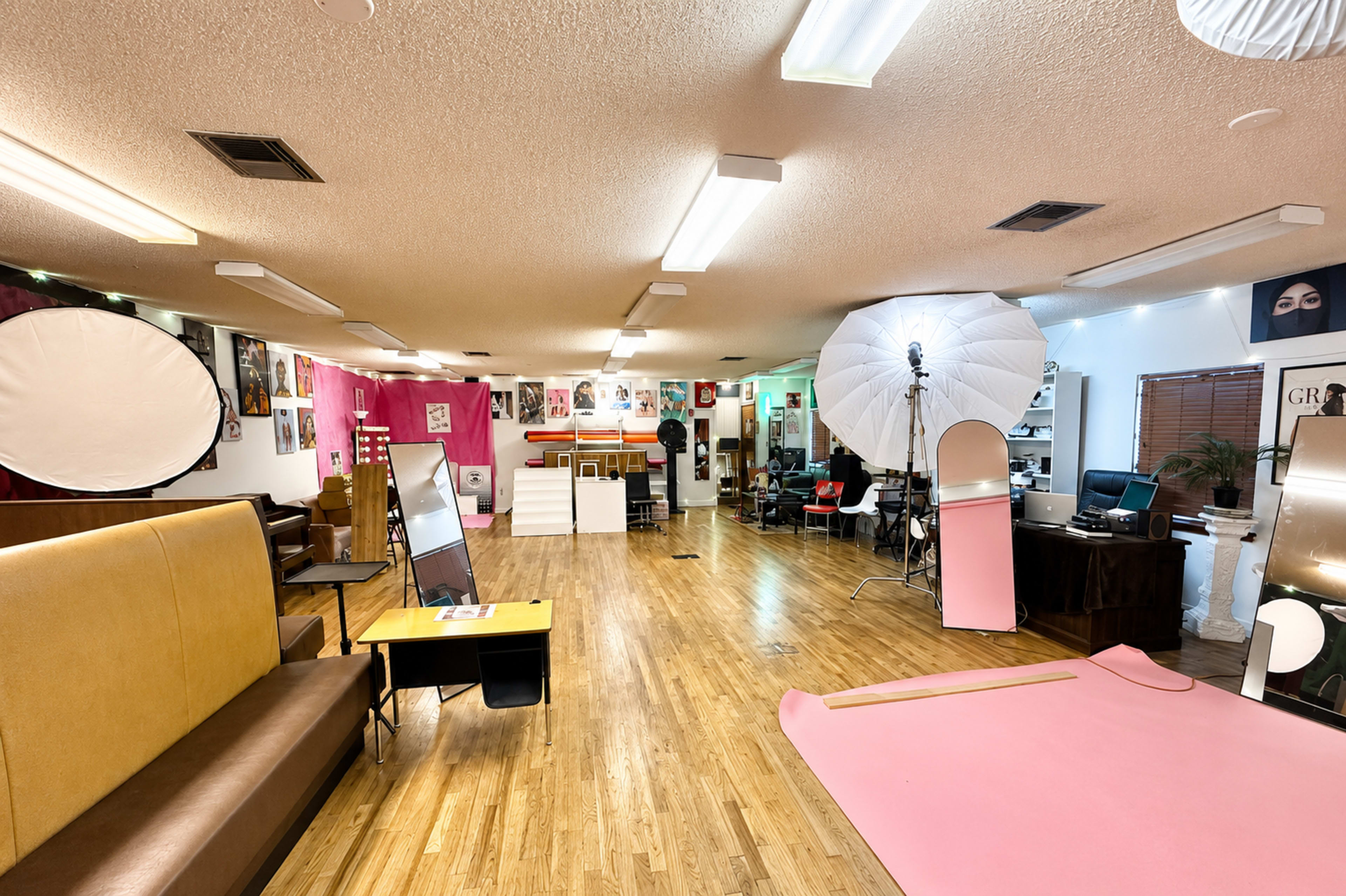 The image shows an interior studio space designed for photography, featuring various lighting equipment, a pink backdrop, and seating areas.