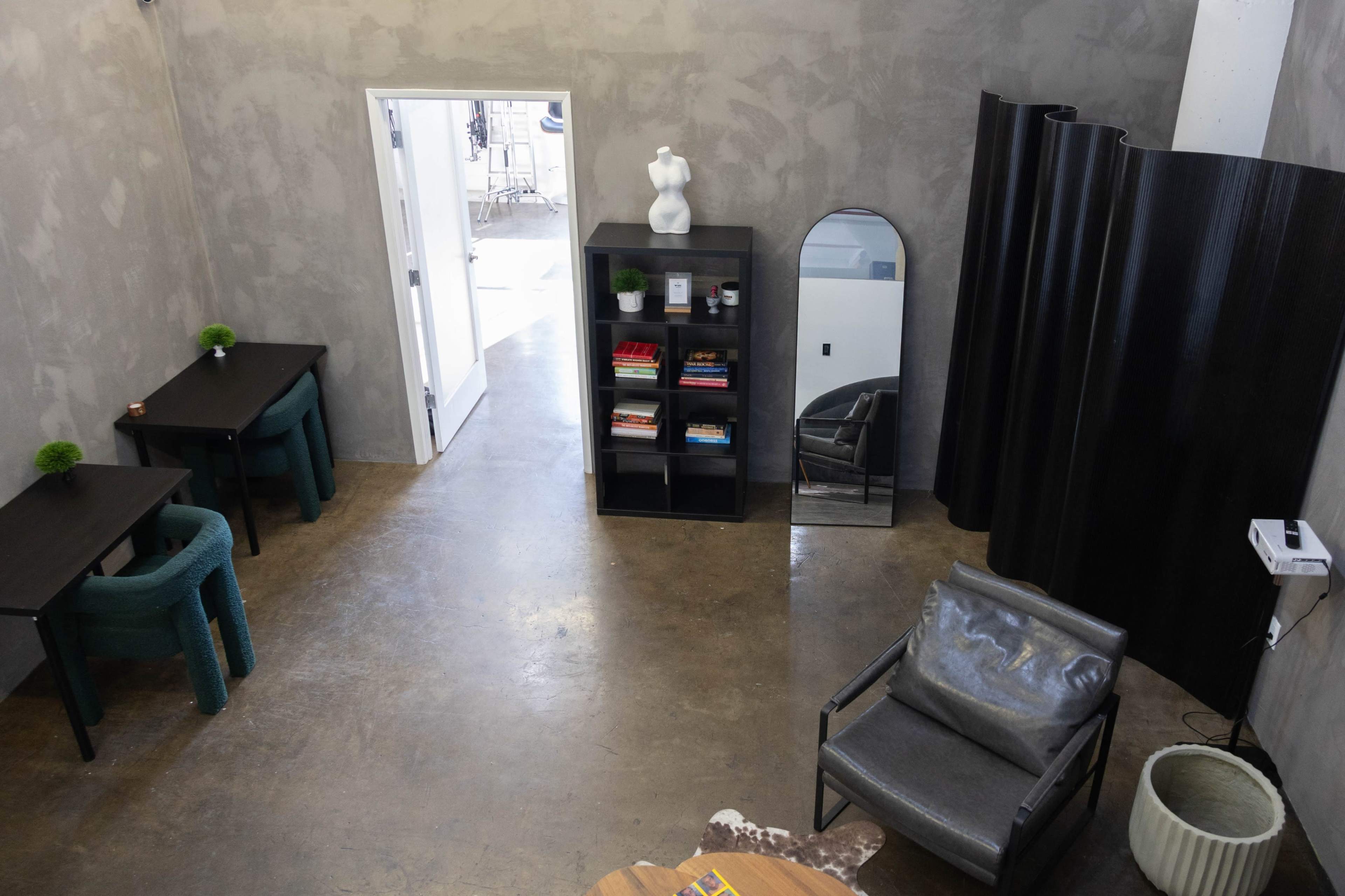 The image shows a modern interior space with a minimalist design, featuring two tables, a bookshelf, a large mirror, and a curved black partition.