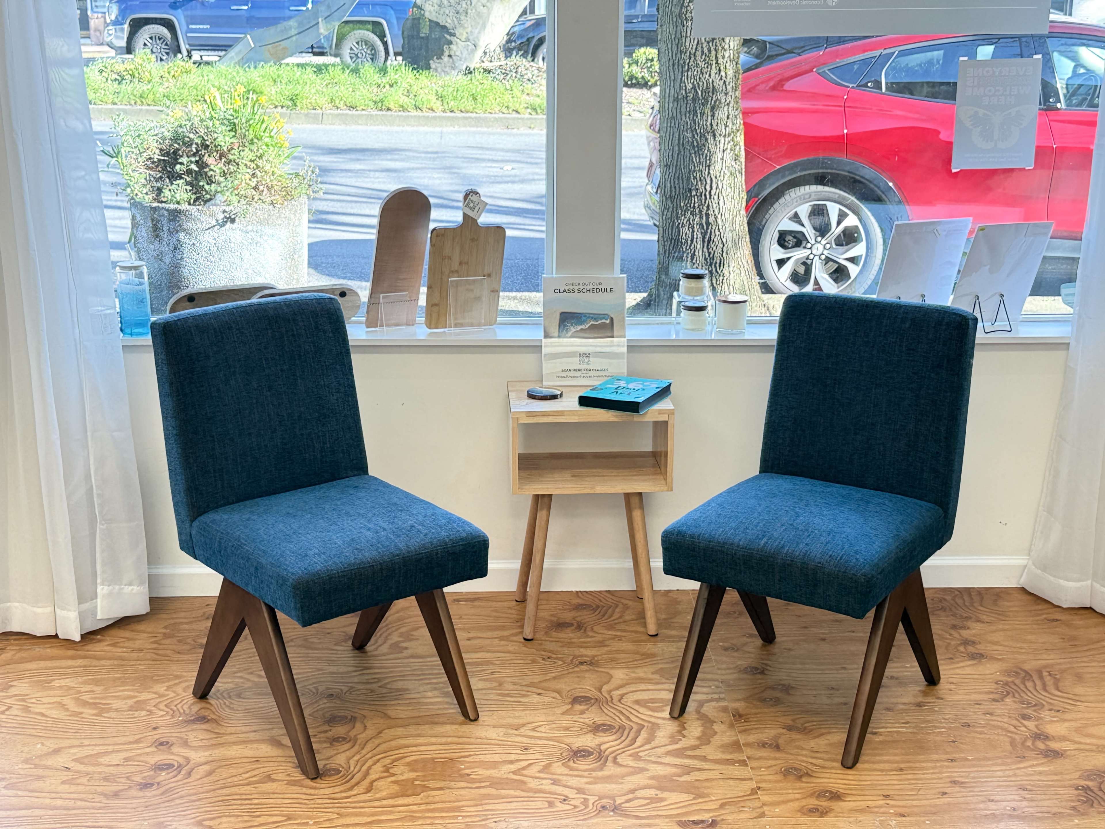 Two upholstered chairs sit opposite each other in front of a window, alongside a small wooden side table displaying books and decorative items.