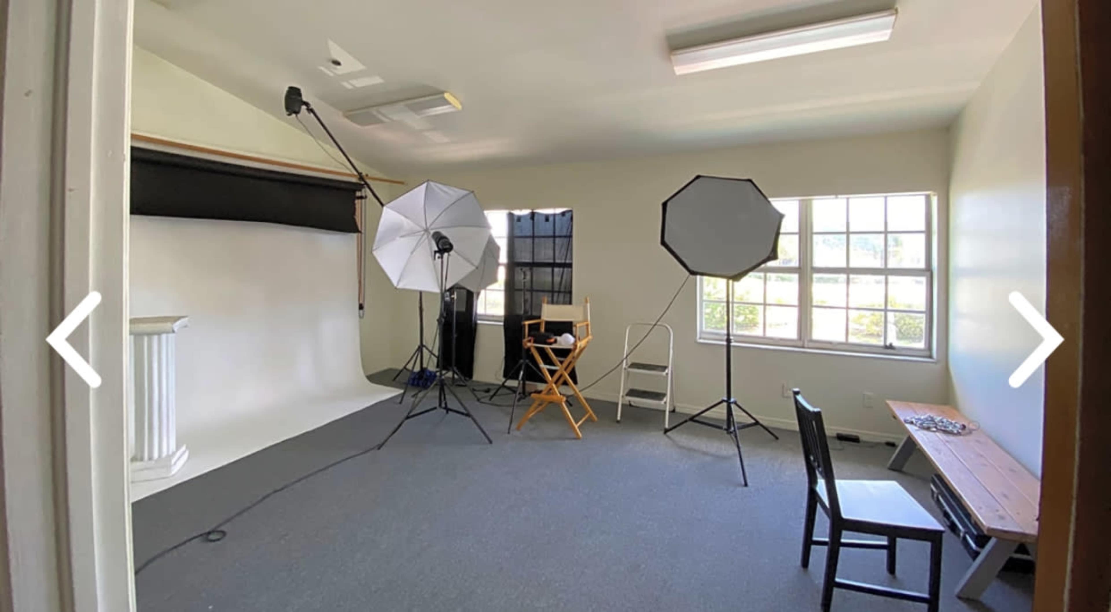 The image shows a photography studio with a backdrop, lighting equipment, and chairs arranged for a photo shoot.
