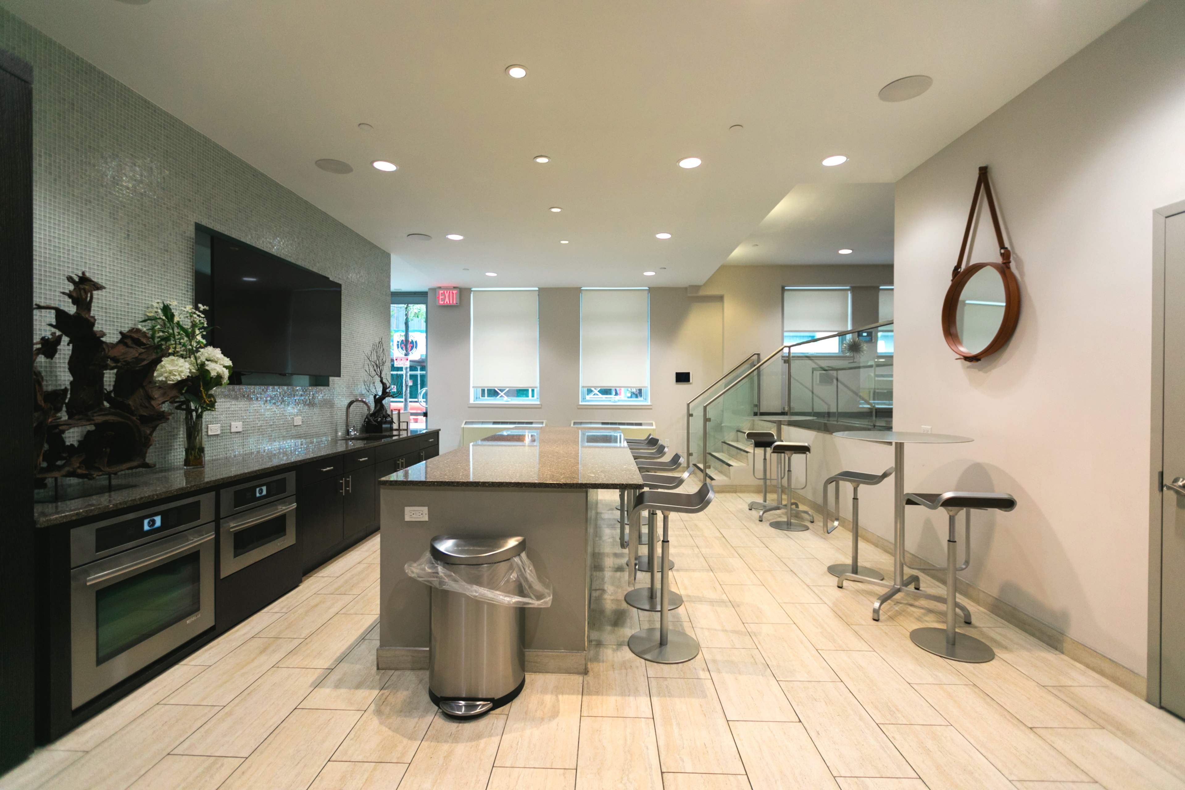 The image shows a modern kitchen and dining area with a large island, bar stools, and a dining table, all featuring sleek furnishings and appliances.