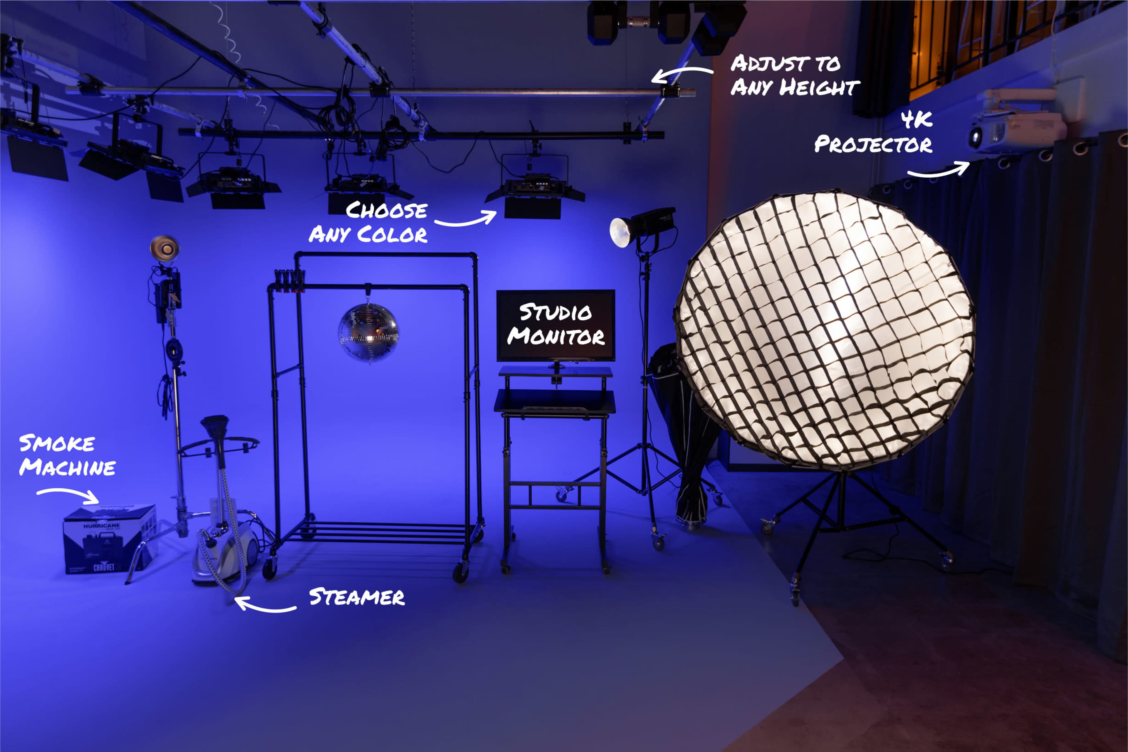 The image shows a studio setup featuring various lighting equipment, a smoke machine, a steamer, a studio monitor, and a projector against a blue background.