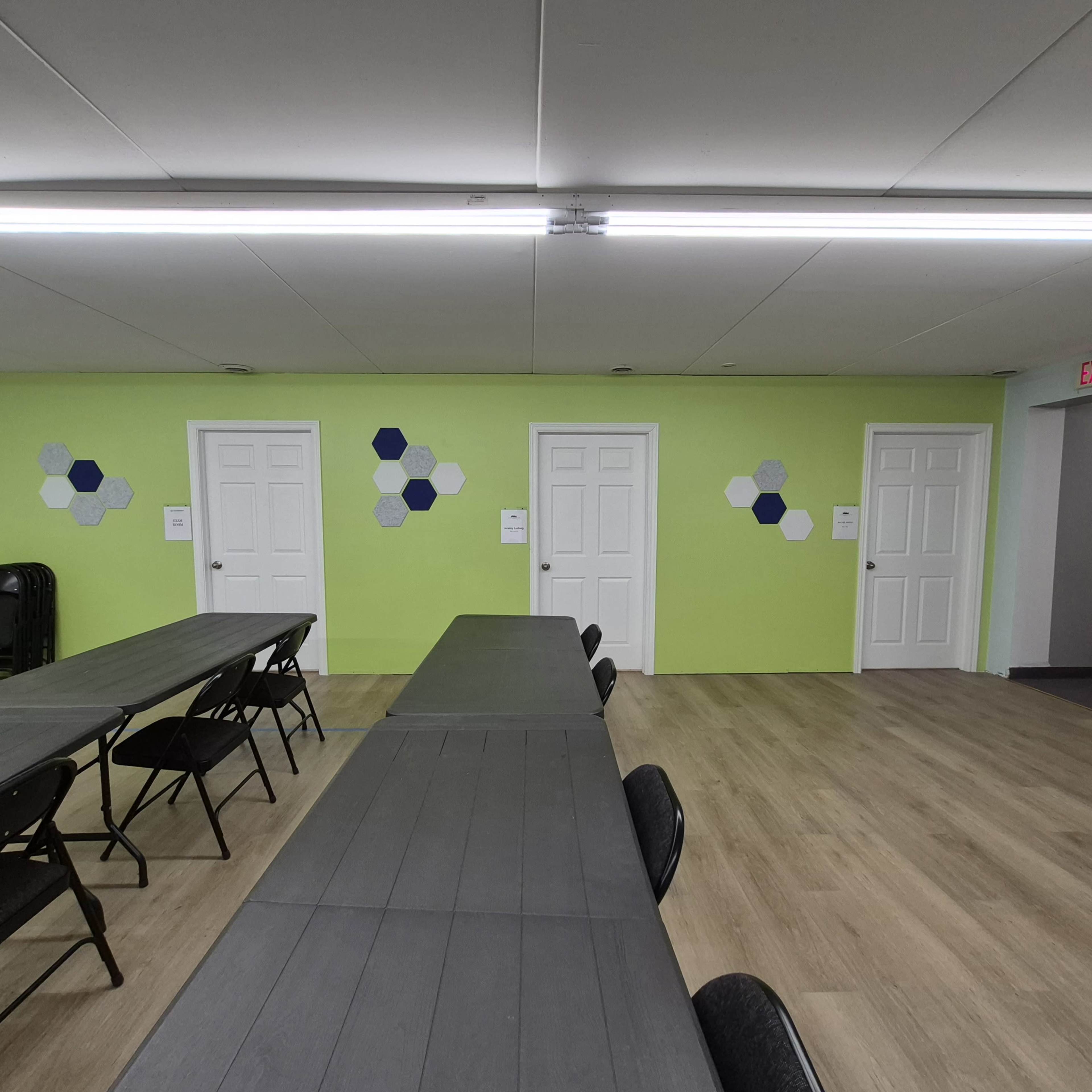 The image shows a room with several tables arranged in a row, green walls featuring hexagonal decorations, and three doors along one side.