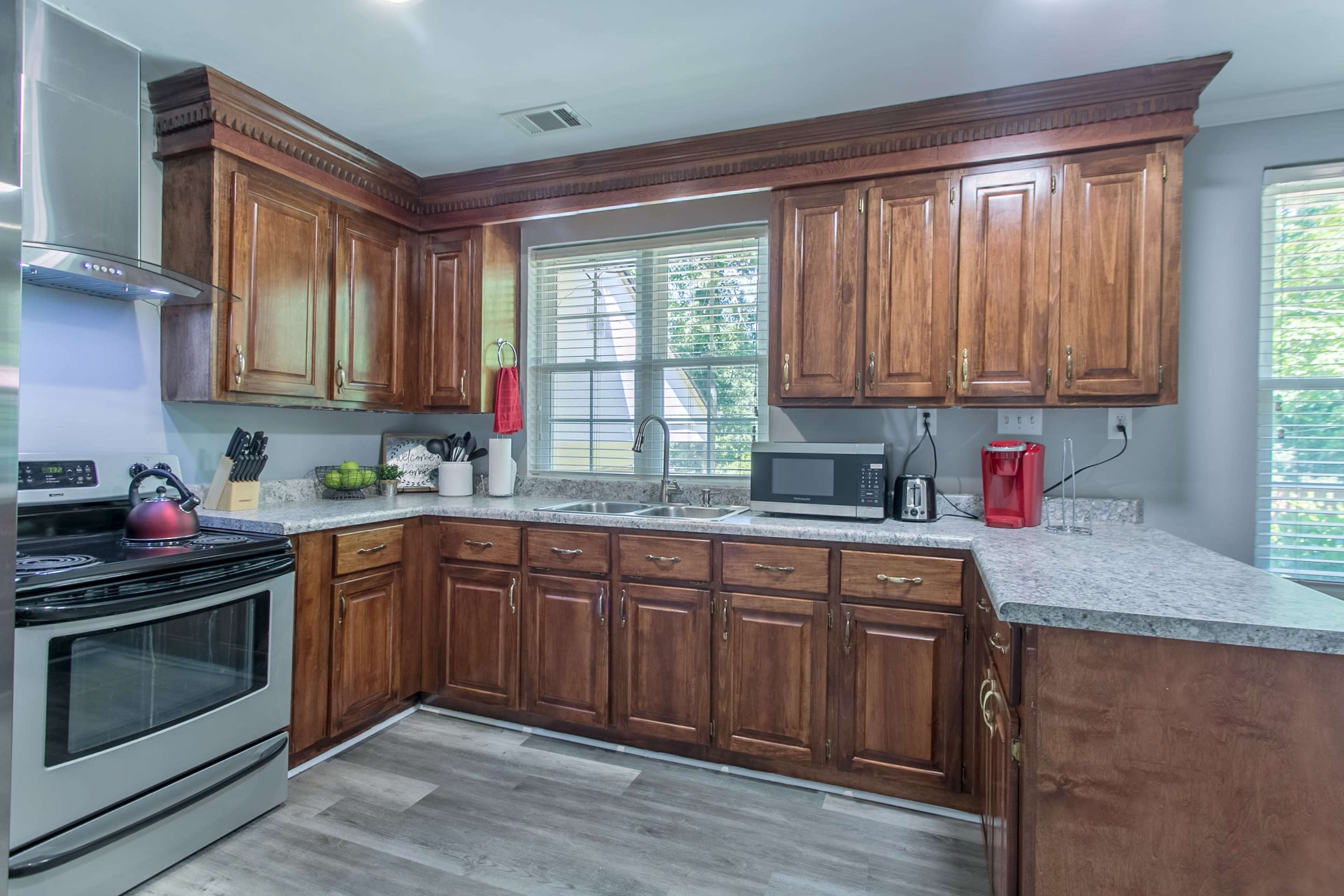 A kitchen with wooden cabinets, a stainless steel oven, and a granite countertop, illuminated by natural light from a window.
