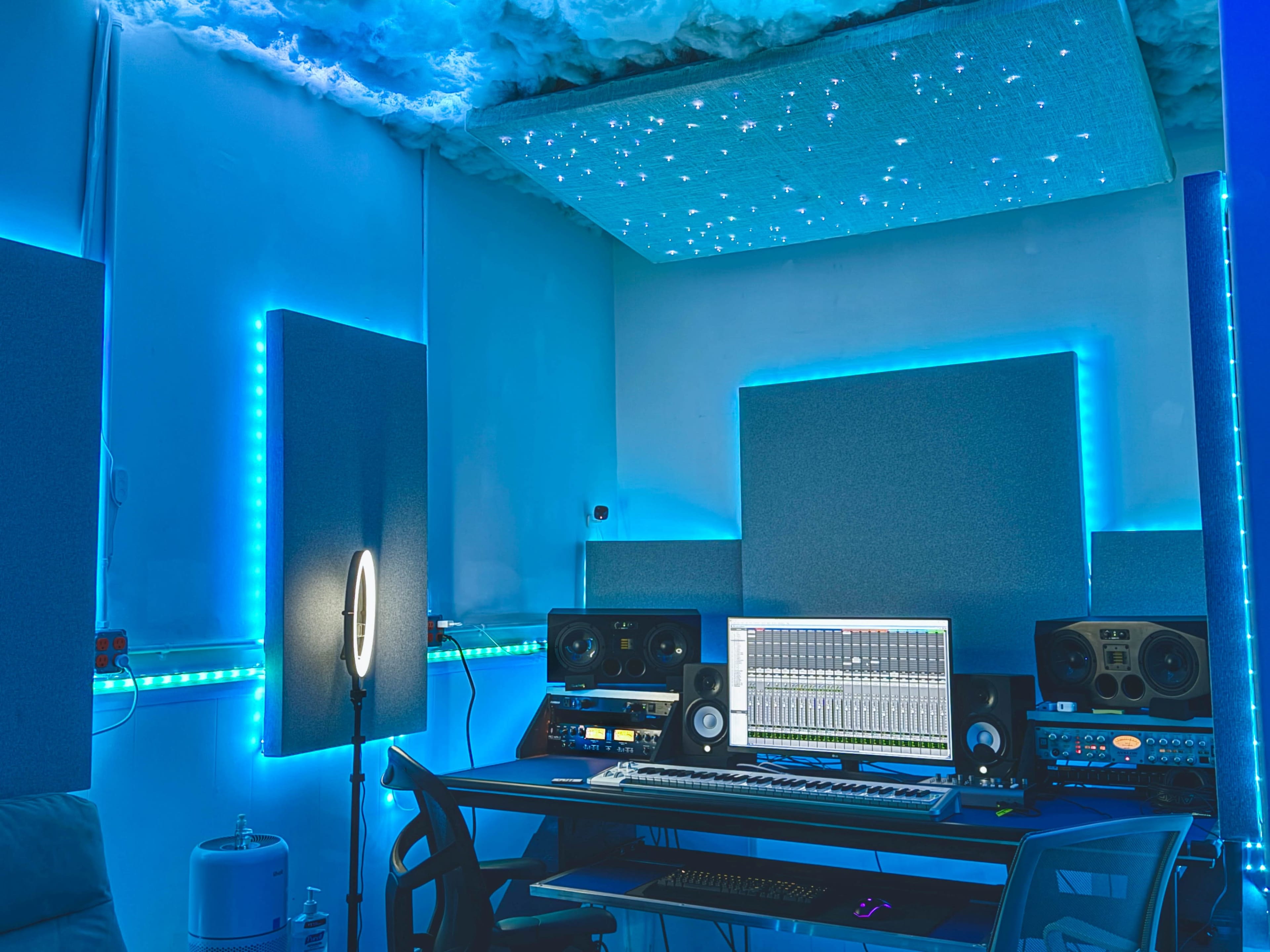 A recording studio with blue LED lights, a digital audio workstation on a desk, and soundproofing panels on the walls.