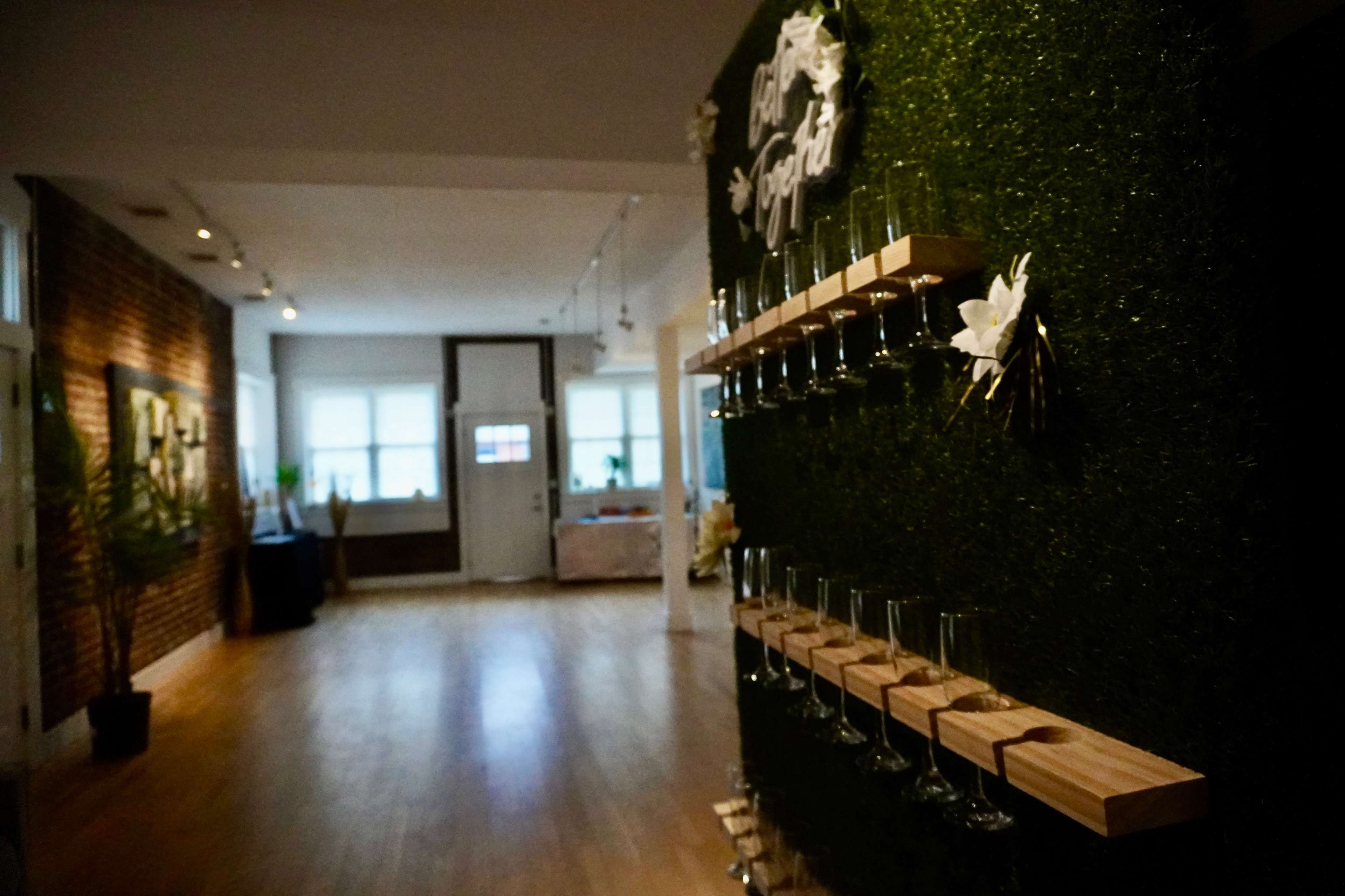 A well-lit interior space featuring a green wall with glass holders and a wooden shelf, leading toward an open area with natural light.