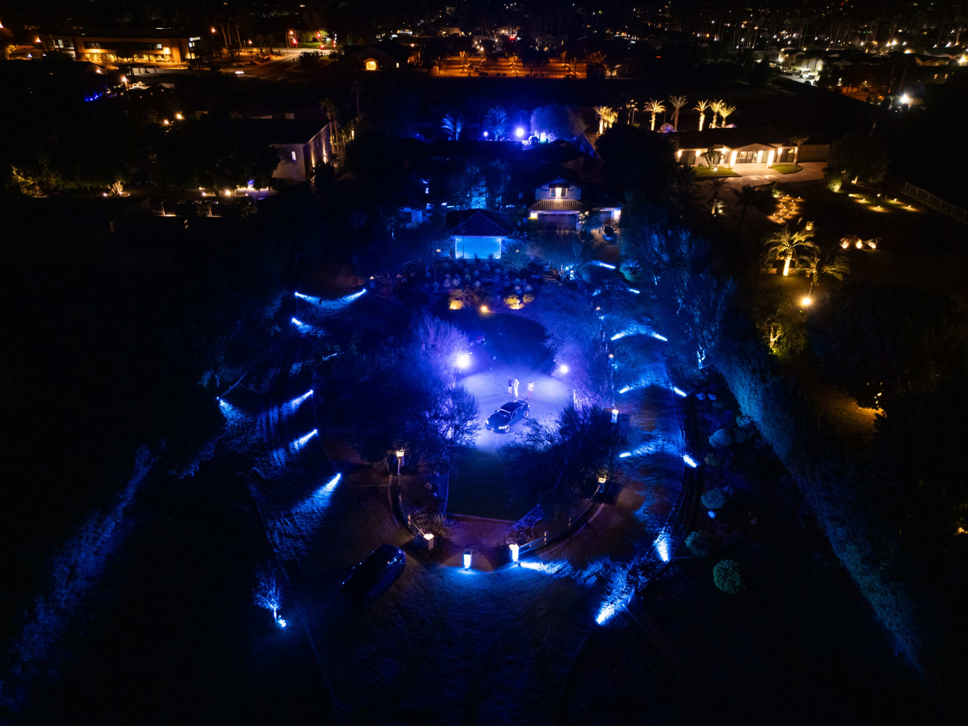 The image shows an aerial view of a landscaped area illuminated by blue lights, with several trees and structures visible in the surroundings.
