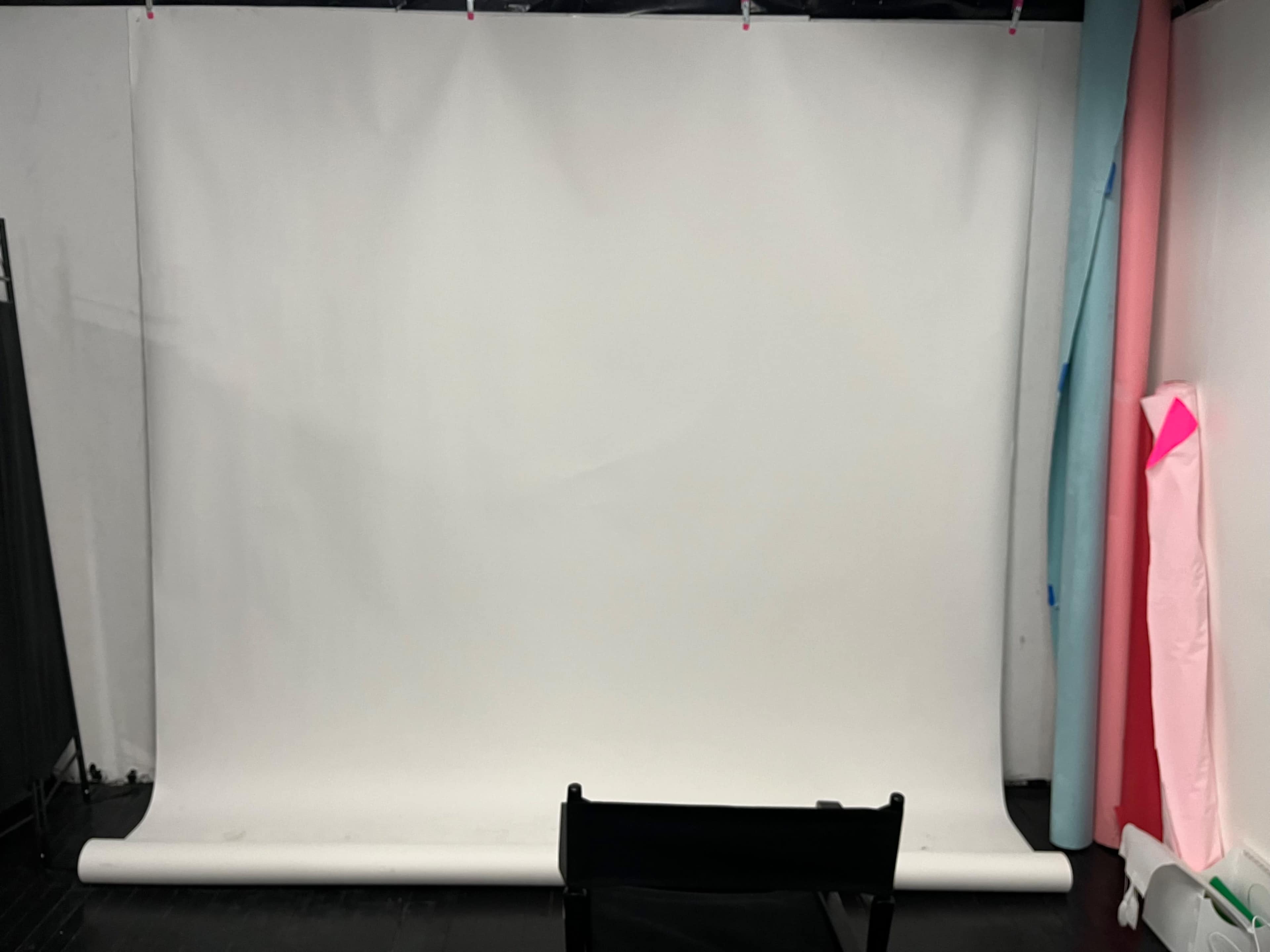 The image shows a plain white backdrop set up in a studio, with a black chair in front and colorful rolls of paper on the side.