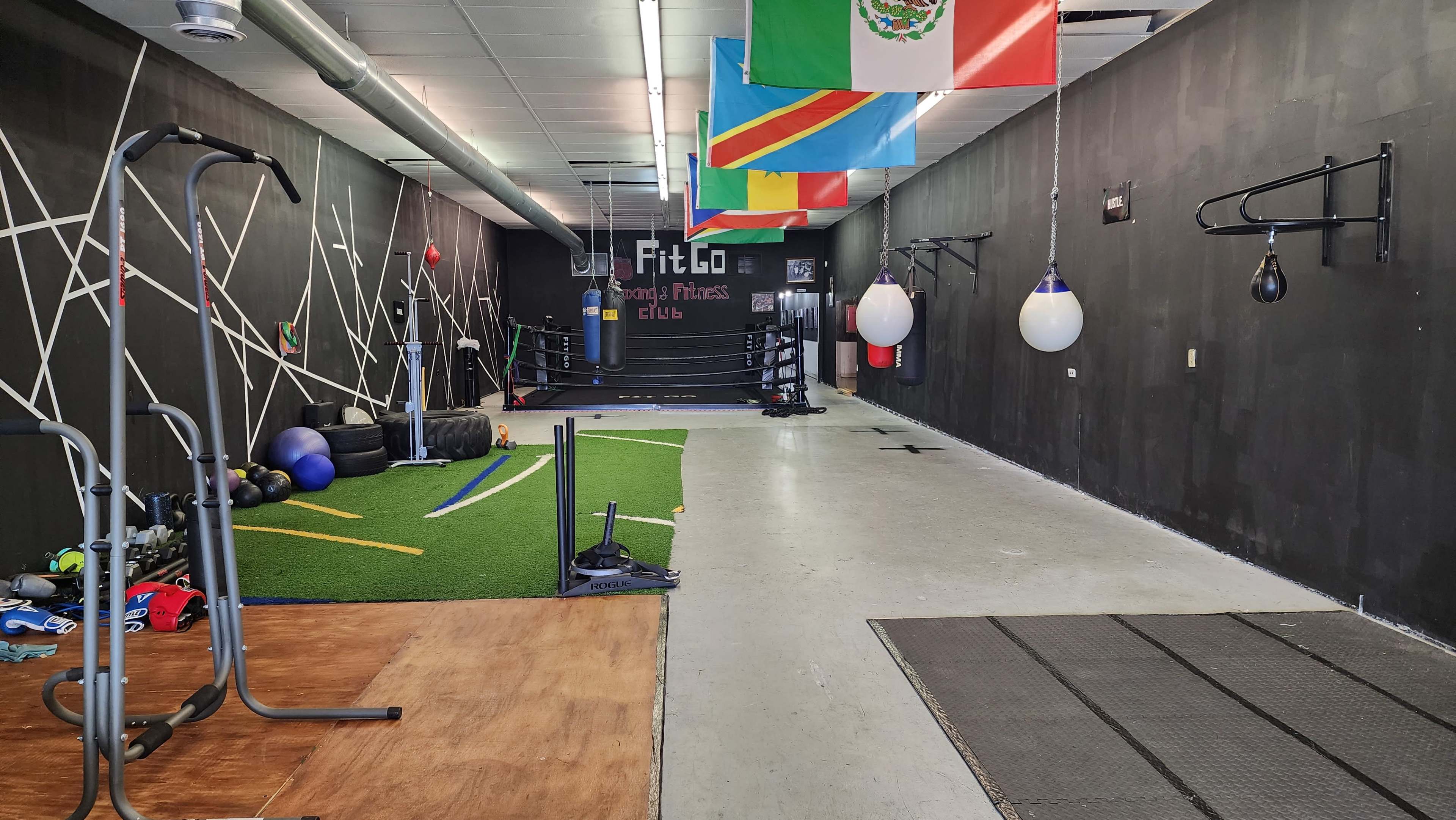 A fitness gym with various exercise equipment, including weights and punching bags, and walls adorned with flags from different countries.