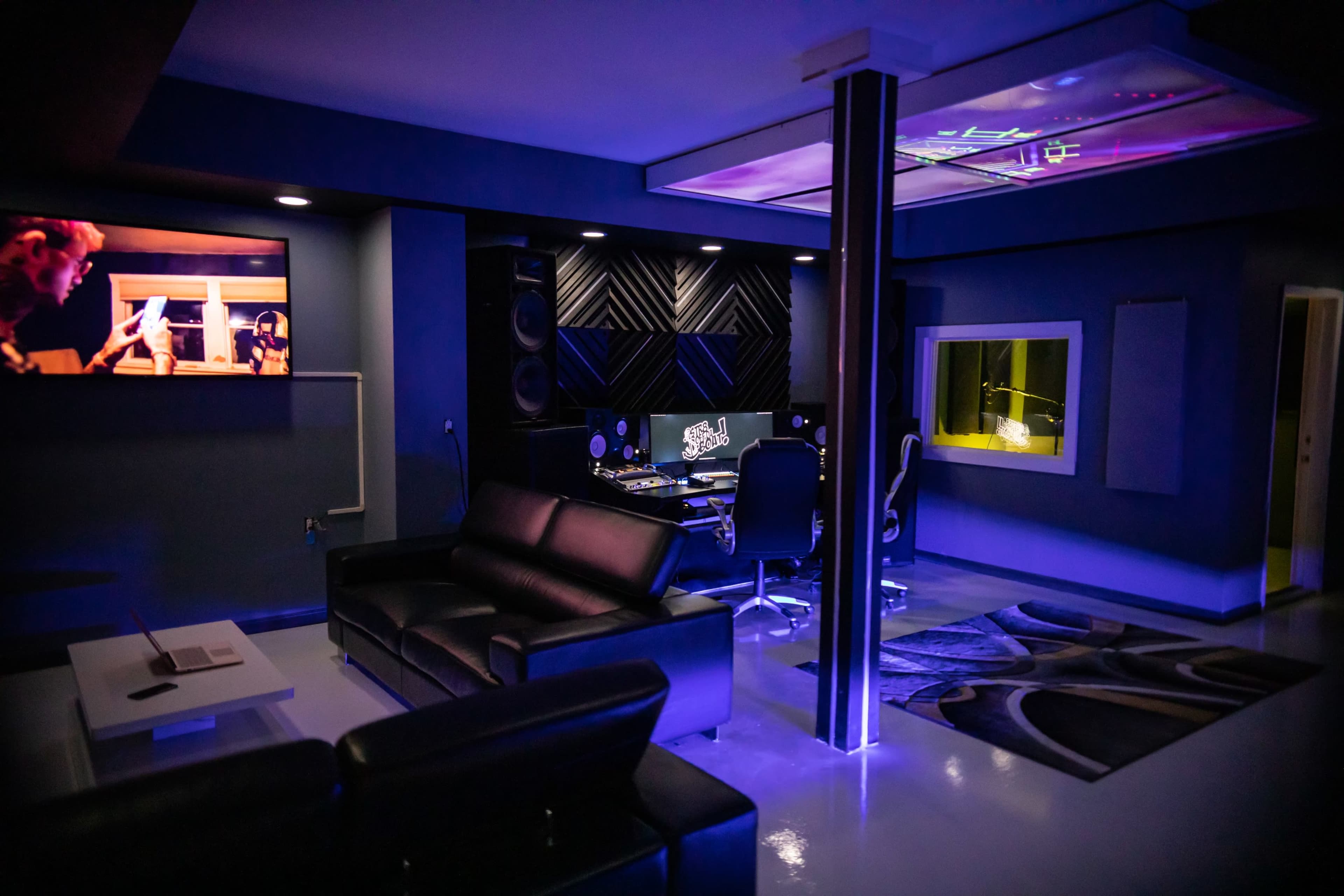 A modern music studio featuring a control room with a mixing console, a comfortable seating area, and ambient lighting.