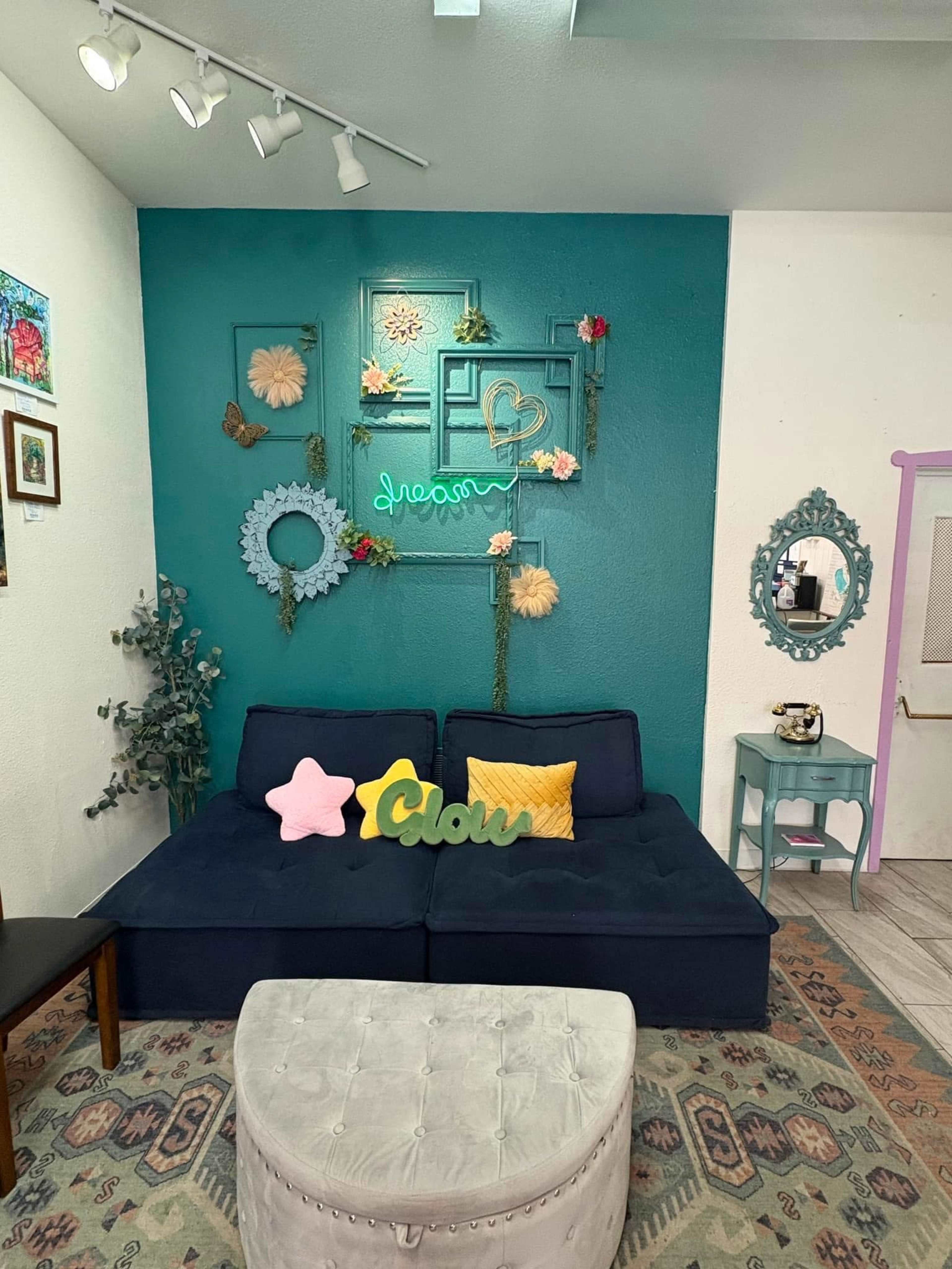 The image shows a cozy seating area with a blue wall adorned with decorative elements, including plants and colorful signs, along with a dark blue couch and a light-colored ottoman.
