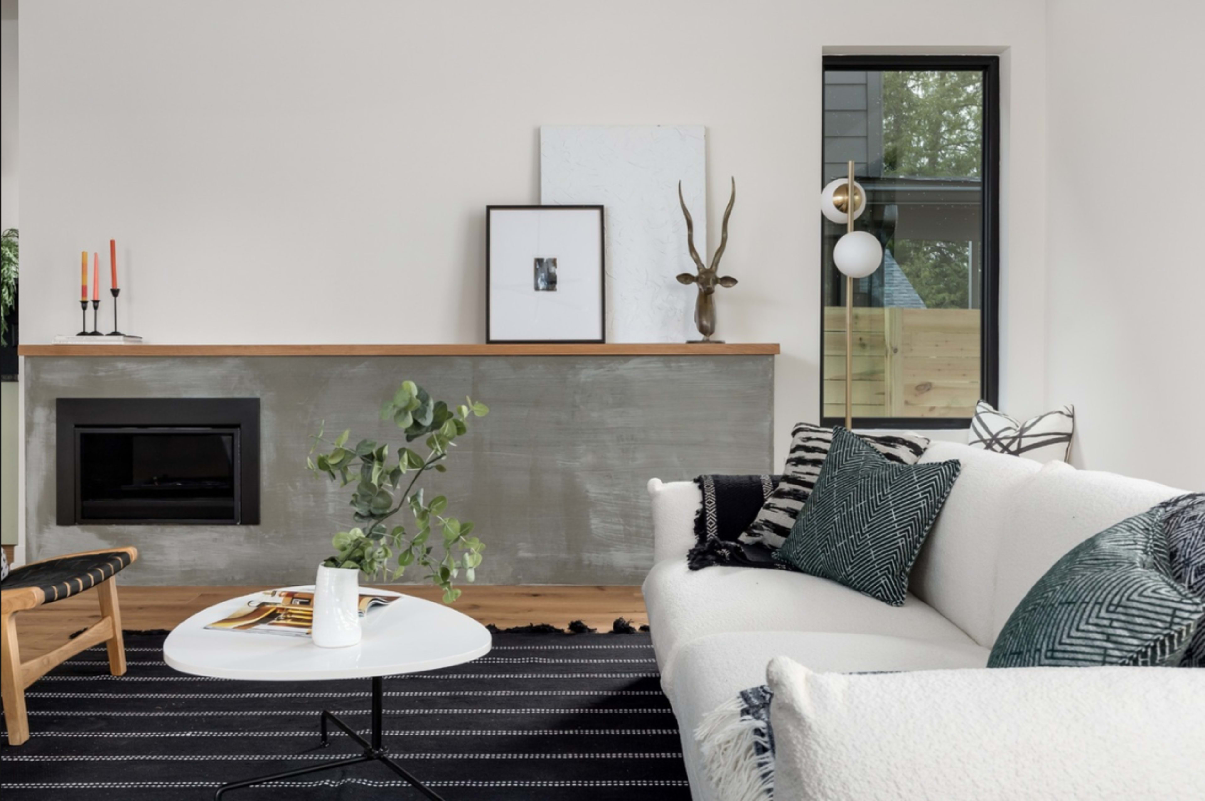 A modern living room features a light sofa, a coffee table, and a fireplace with decorative elements on a concrete mantel.