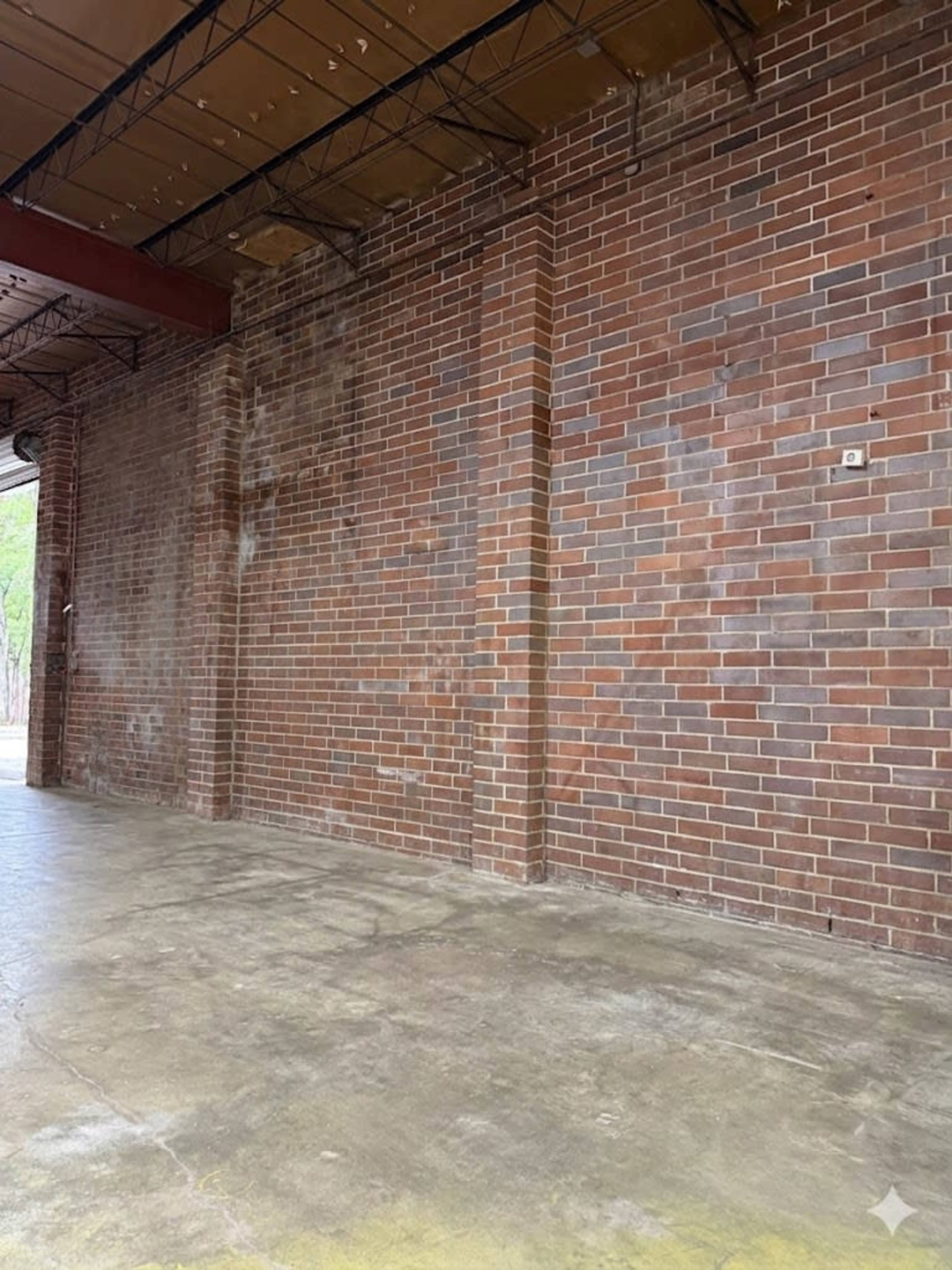 The image shows a large, empty interior space with bare brick walls and a concrete floor.