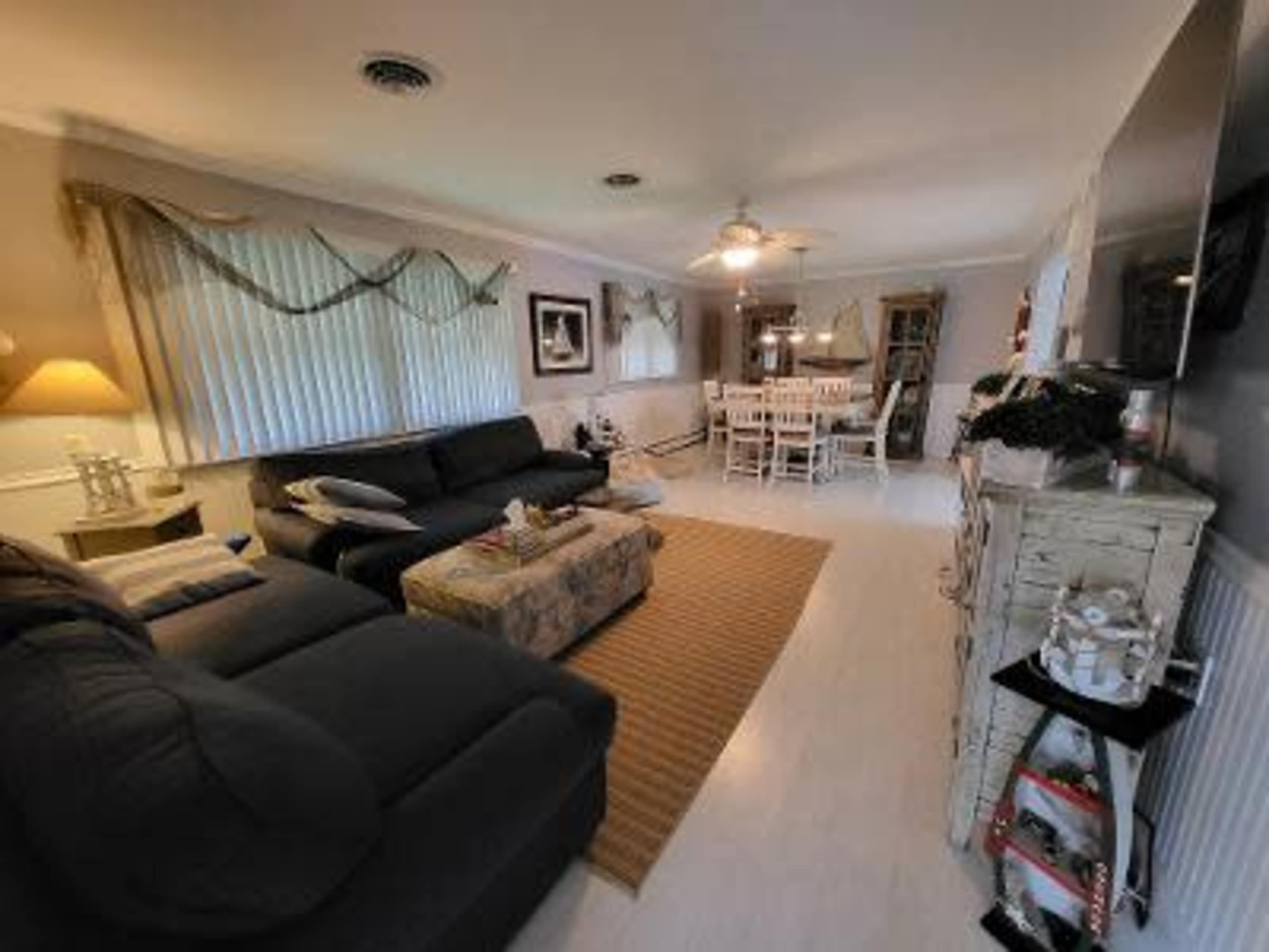 A living room featuring a seating area with two dark sofas, a coffee table, and a dining set in the background.