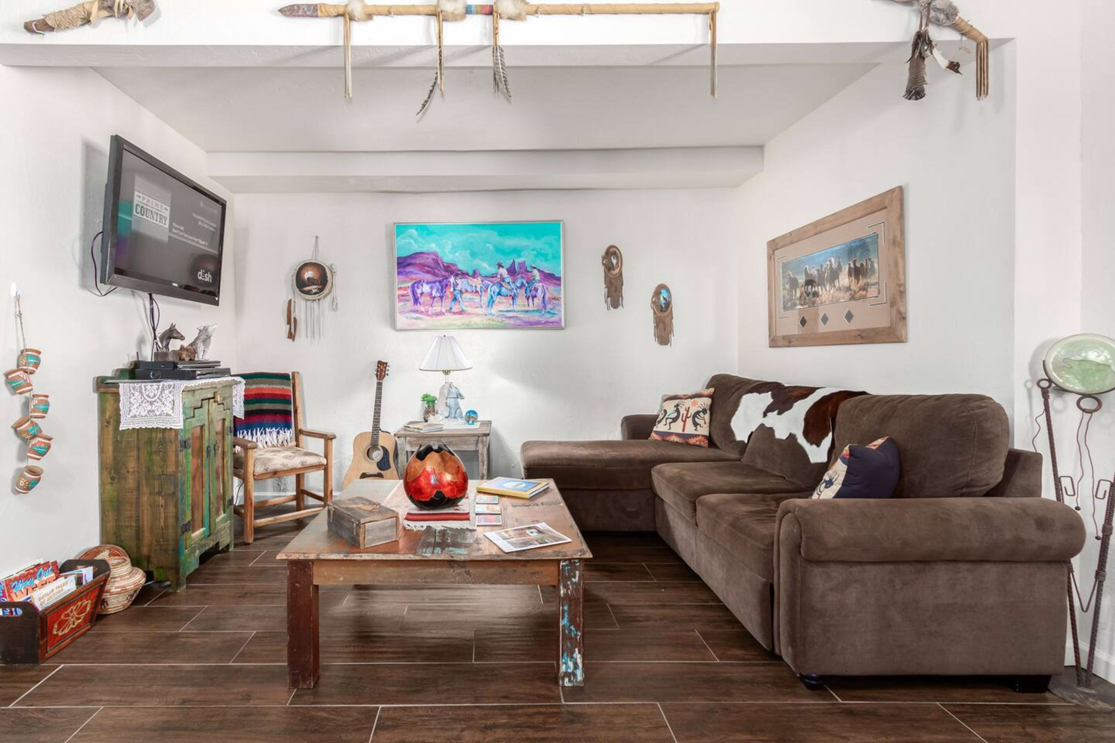A living room with a brown couch, a wooden coffee table, a guitar, and various decorative items on the walls.