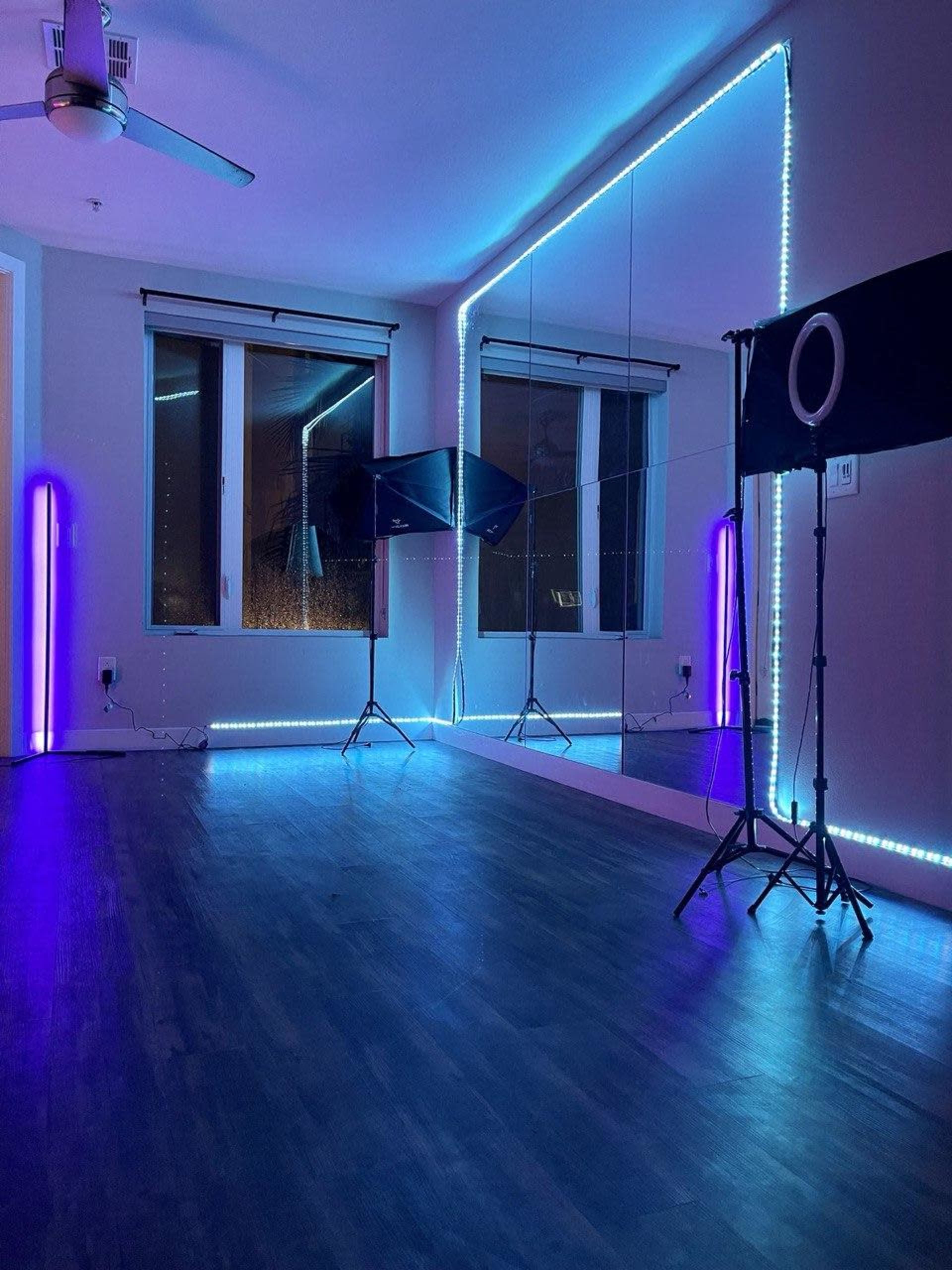 The image shows a modern room with blue and purple LED lighting, featuring a large mirror and photography equipment set up on a wooden floor.