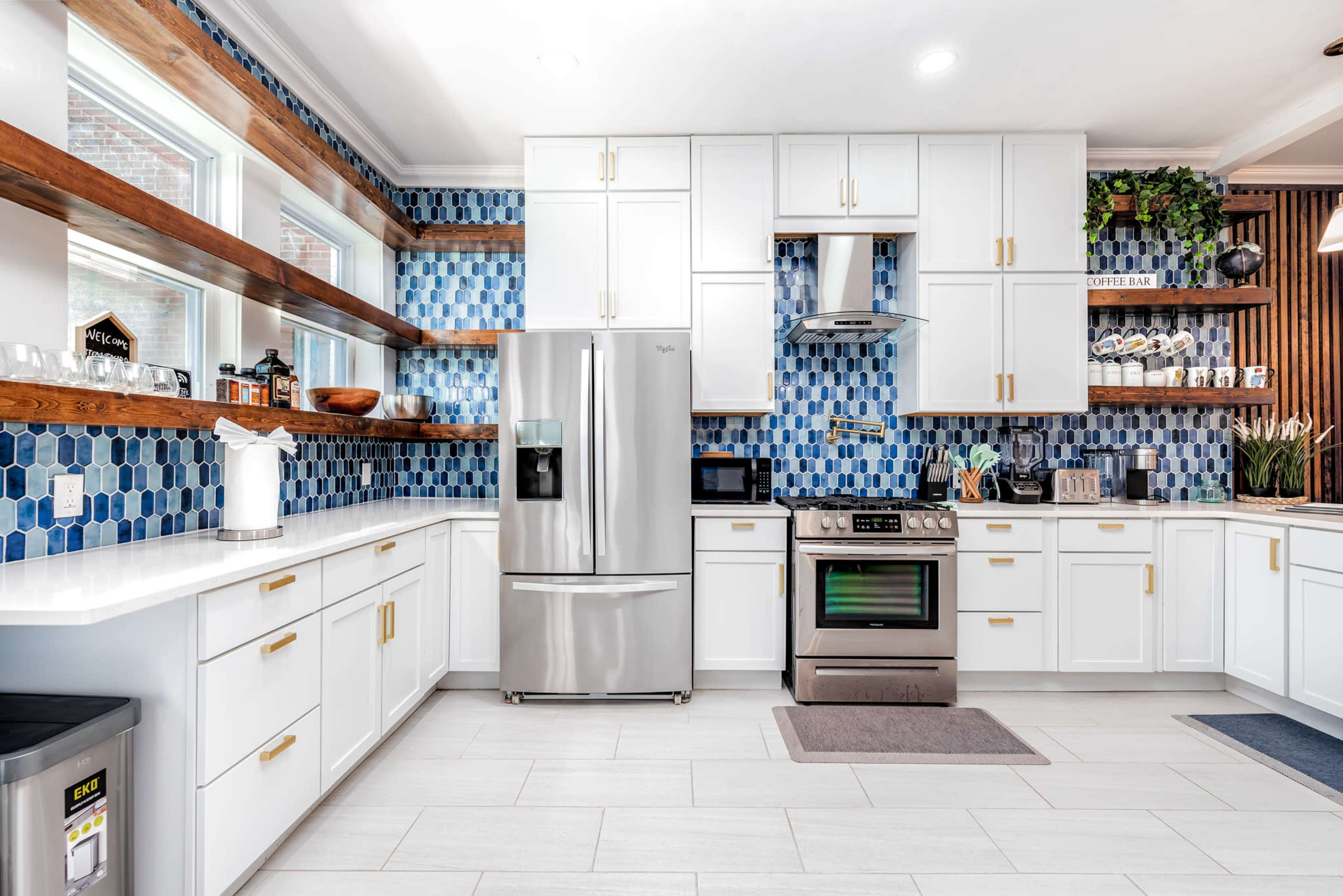 A modern kitchen features white cabinets, a stainless steel refrigerator, and a blue hexagonal tile backsplash.