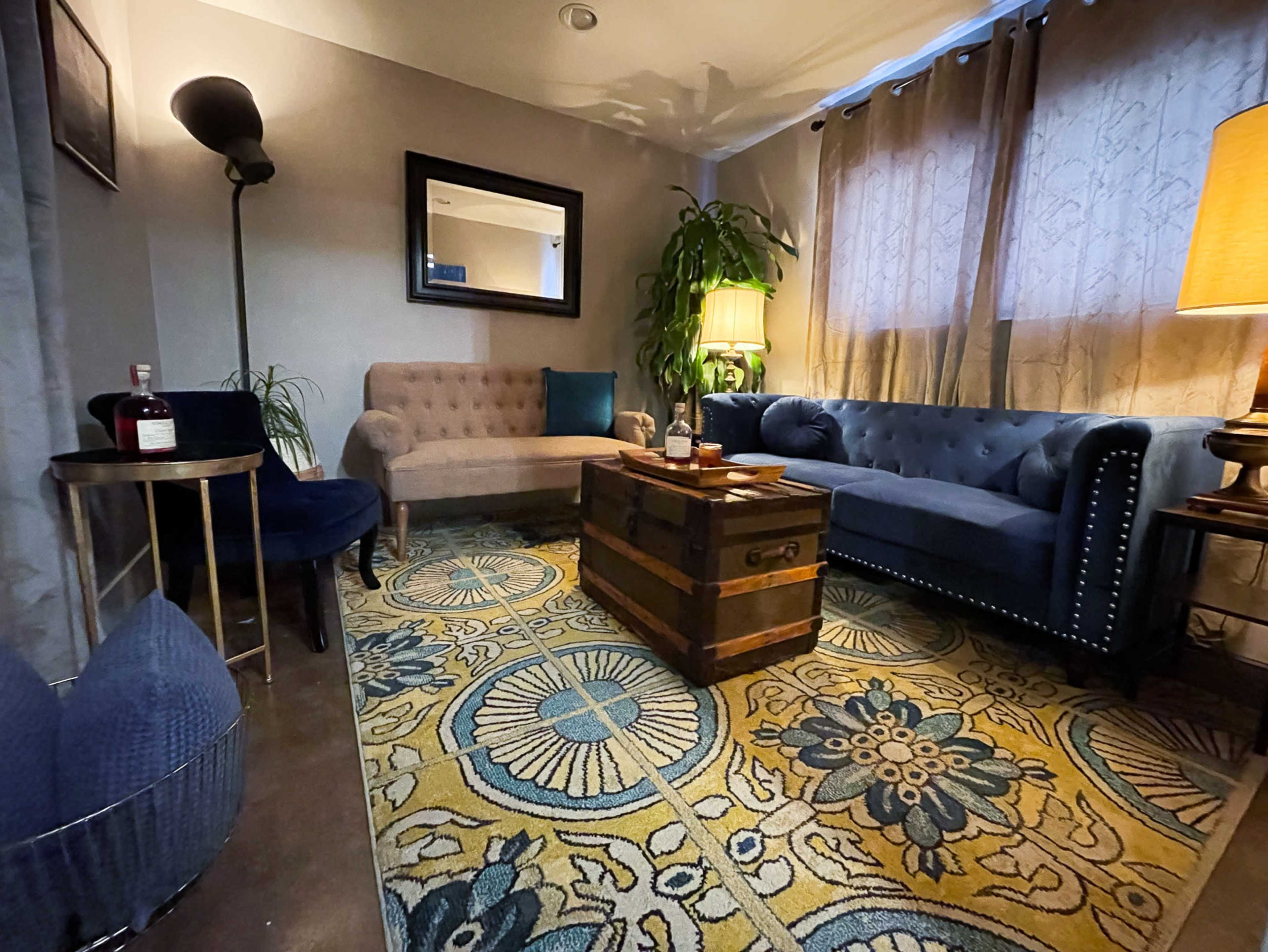 The image shows a cozy living area with a blue chesterfield sofa, a beige loveseat, a wooden coffee table, a floor lamp, and a decorative rug.