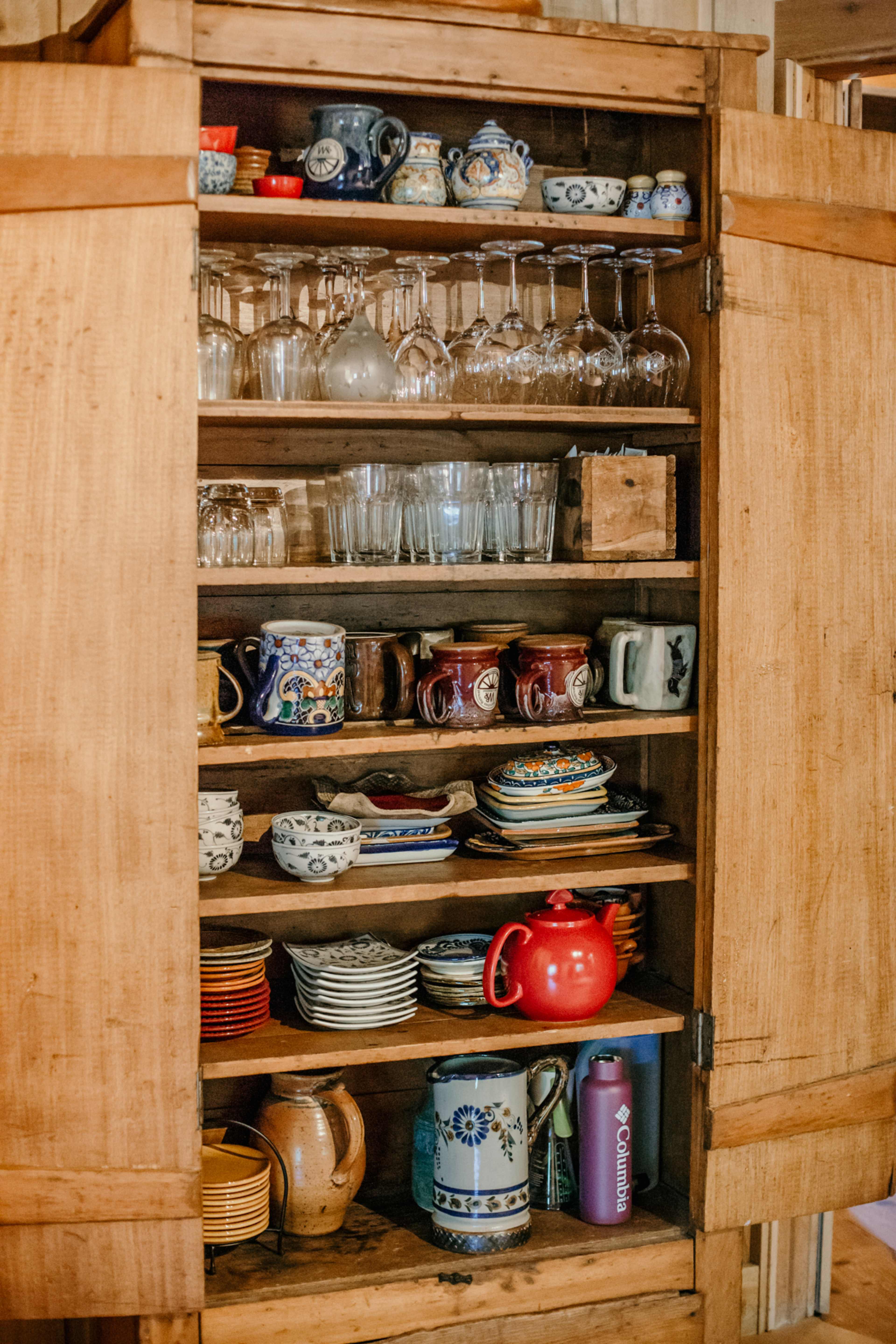 A wooden cupboard displays various types of glassware, mugs, and decorative dishes.