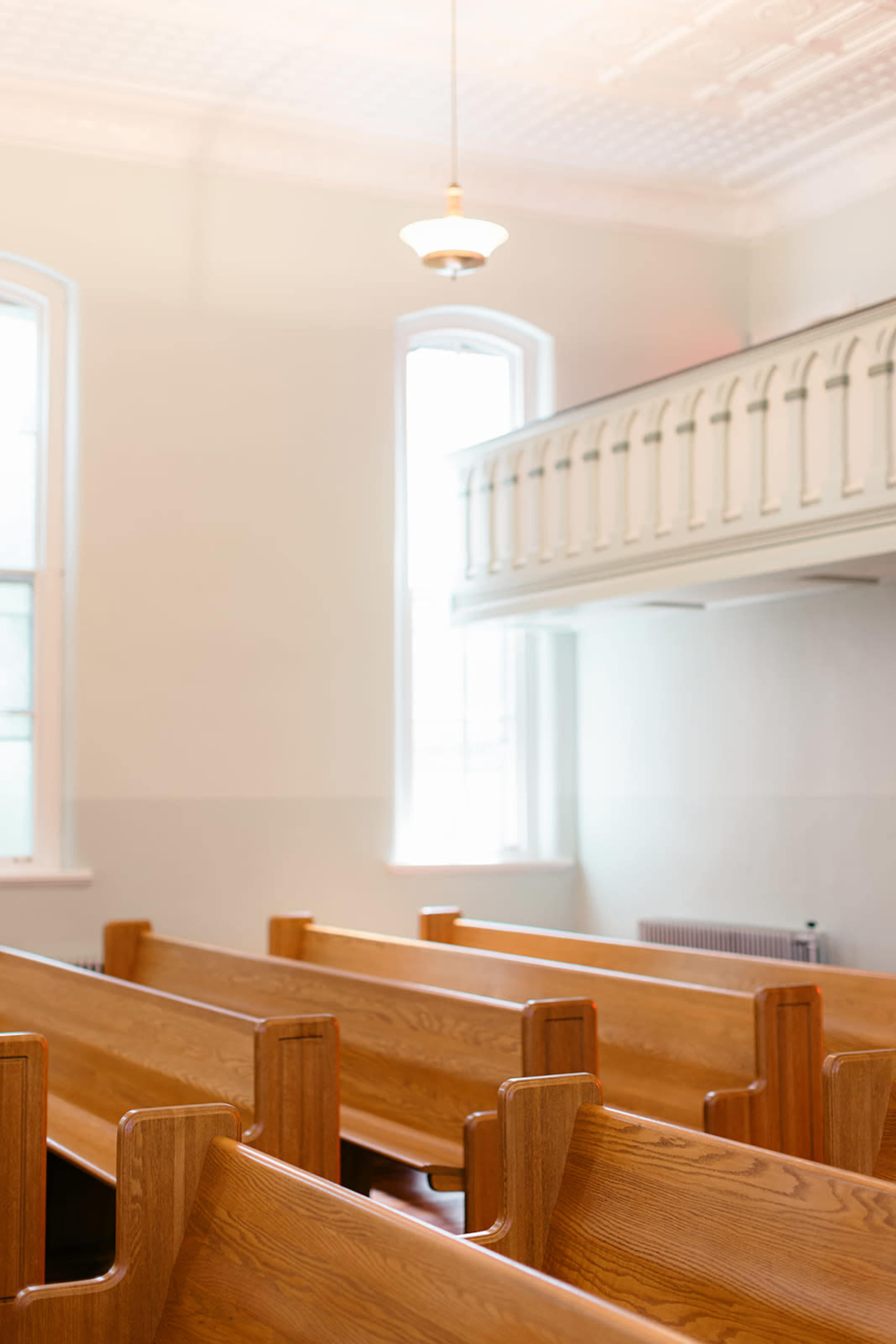 The image shows a row of wooden church pews facing a balcony and windows in a light-colored interior space.