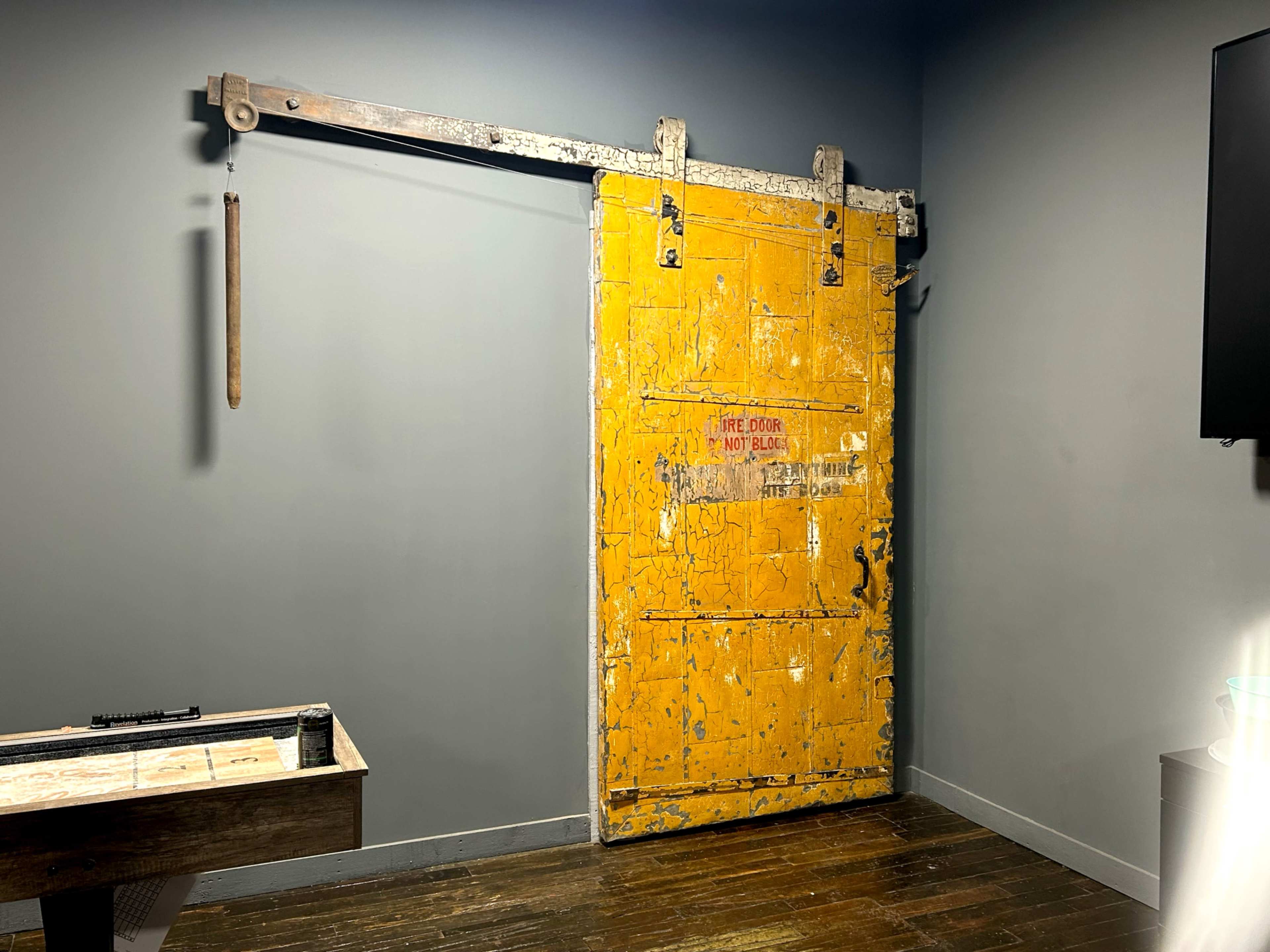 The image features a large, weathered yellow sliding barn door mounted on a gray wall with a metal track.