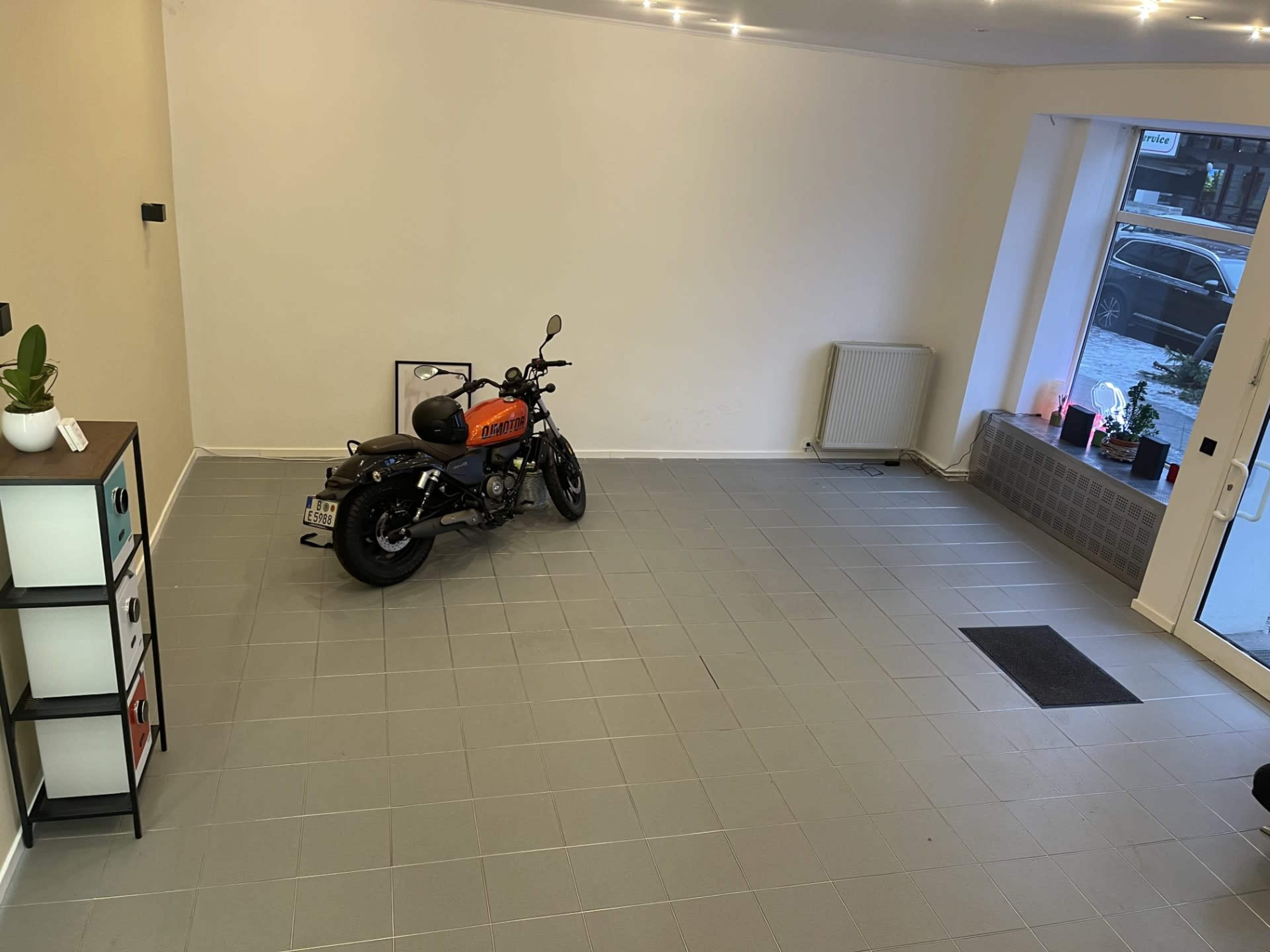 The image shows a spacious, empty garage with a motorcycle parked in one corner, and large windows letting in natural light.