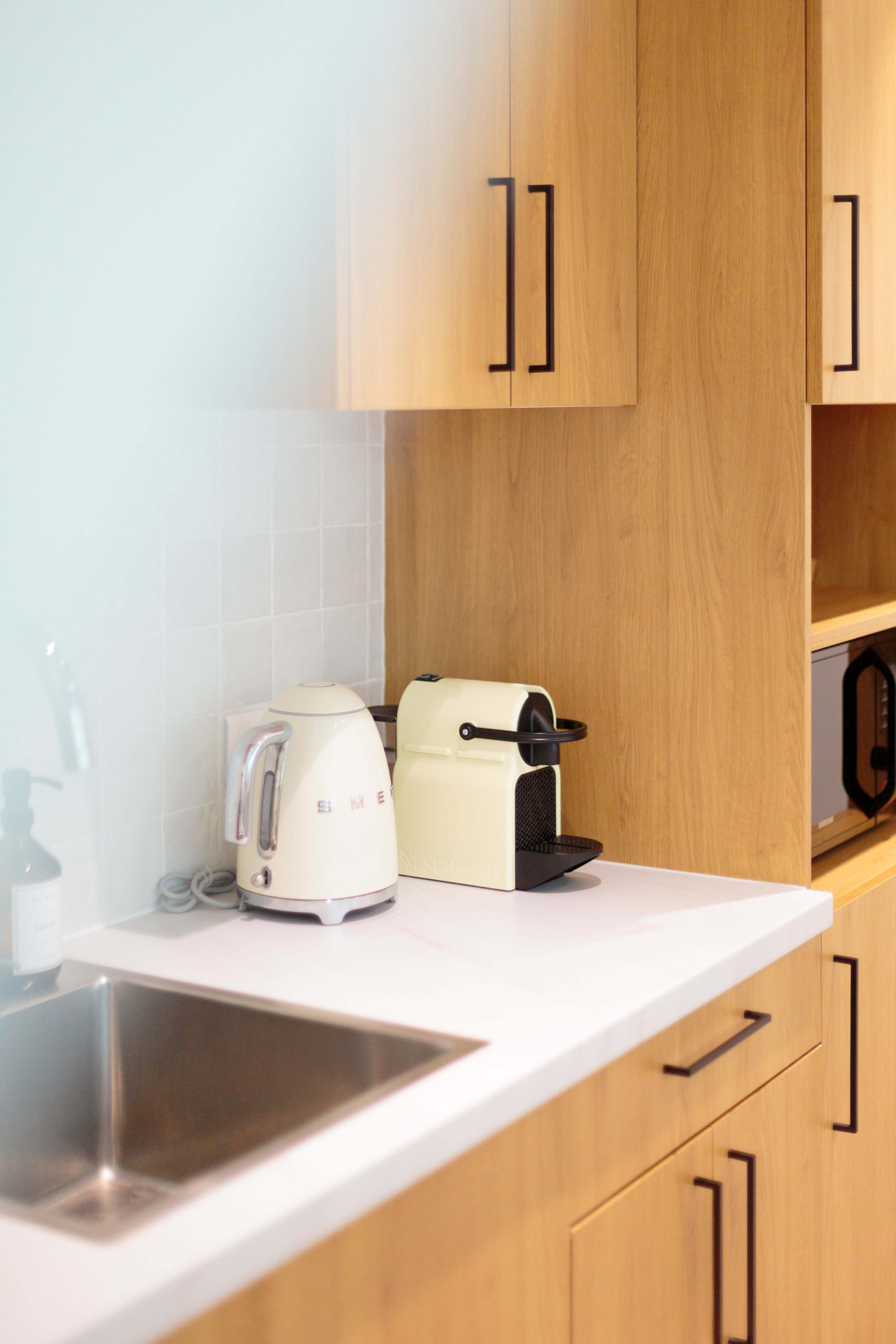 A modern kitchen features wooden cabinetry, a stainless steel sink, a kettle, and a coffee machine on the countertop.