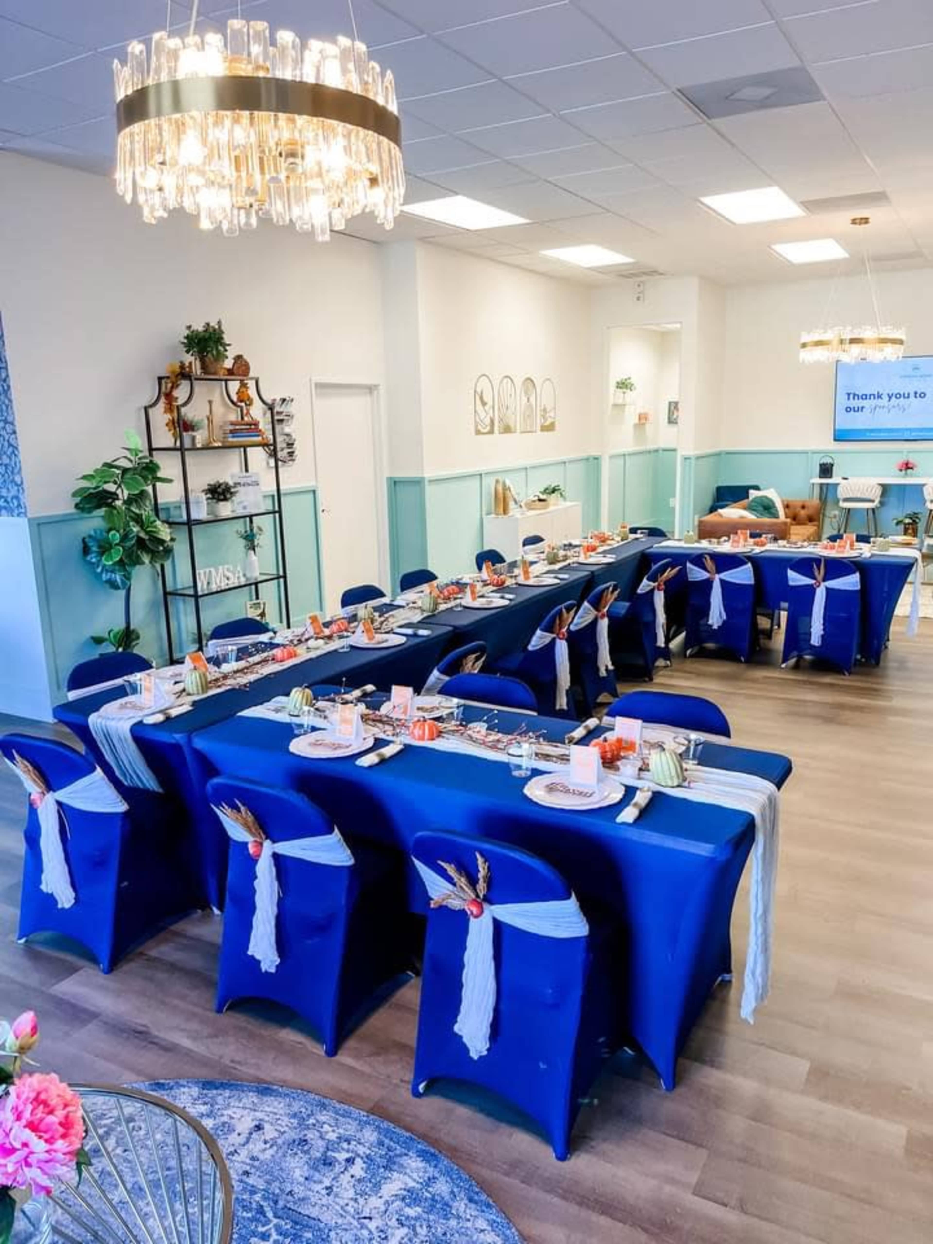 The image shows a decorated dining area with long tables covered in blue tablecloths, set for a meal with colorful centerpieces and dining ware.