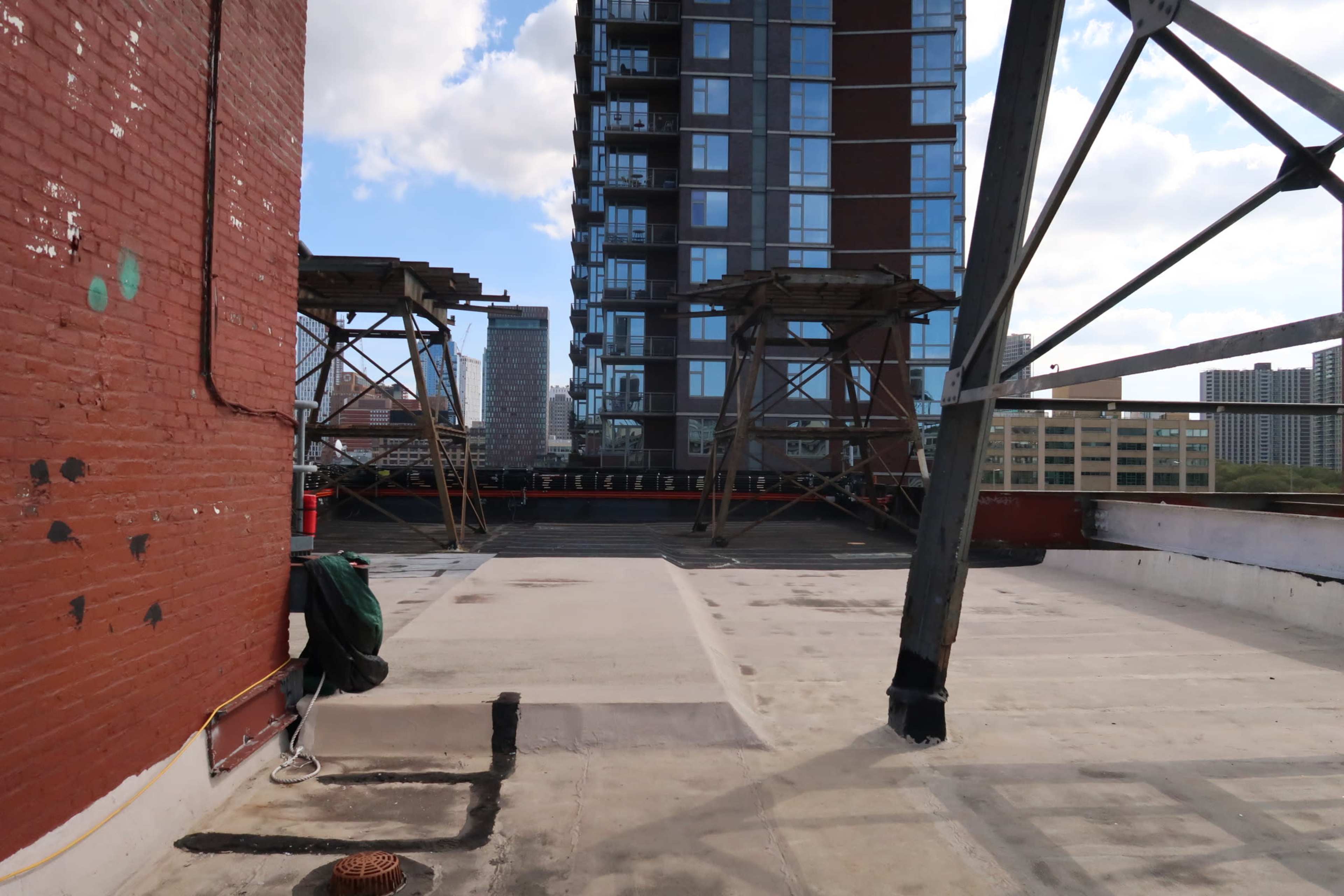 A rooftop area with a concrete surface, industrial support structures, and a tall apartment building in the background.