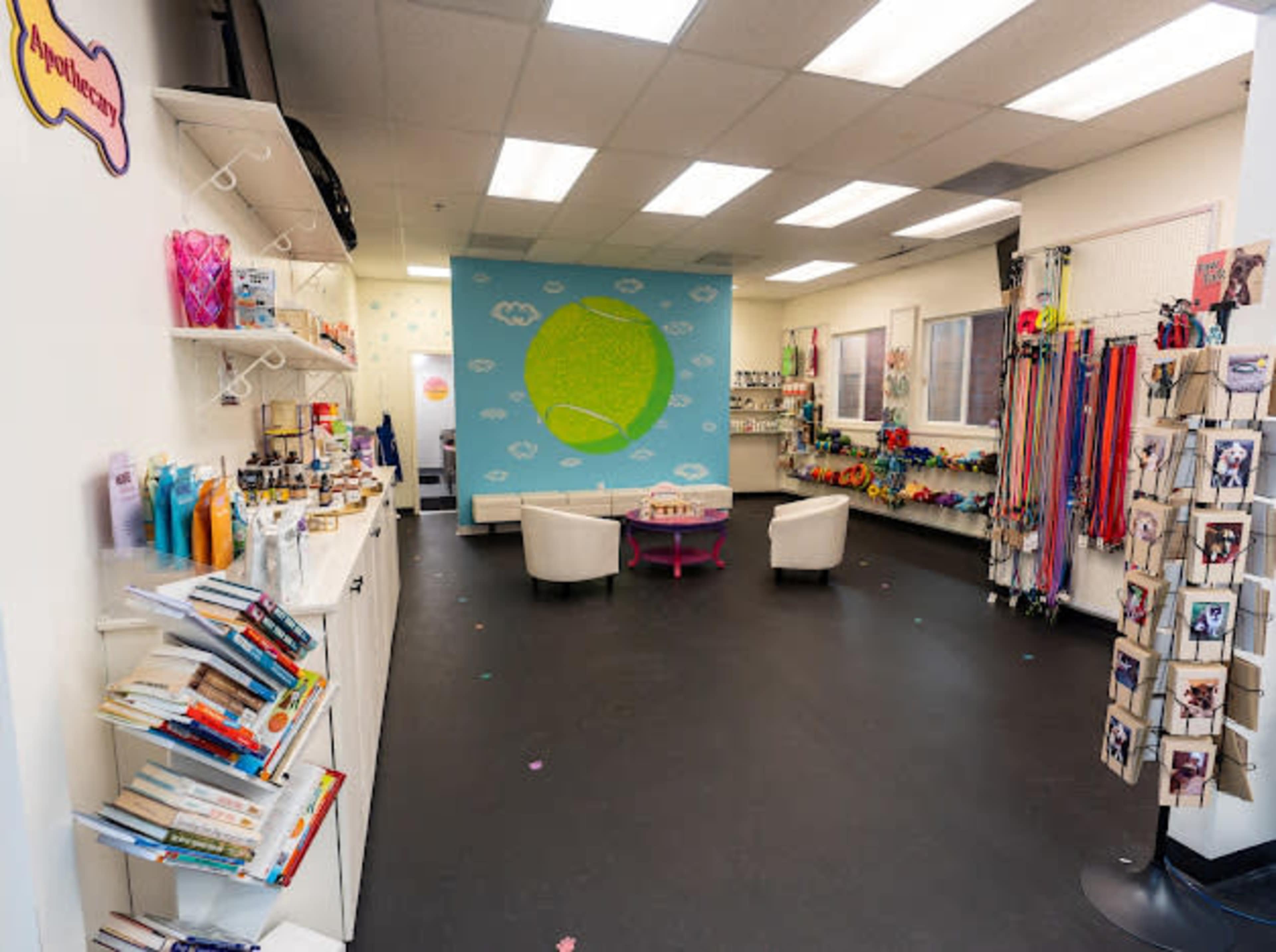 The image shows a brightly lit retail space with white shelves displaying various products, a colorful mural on the wall, and seating arrangements in the center.