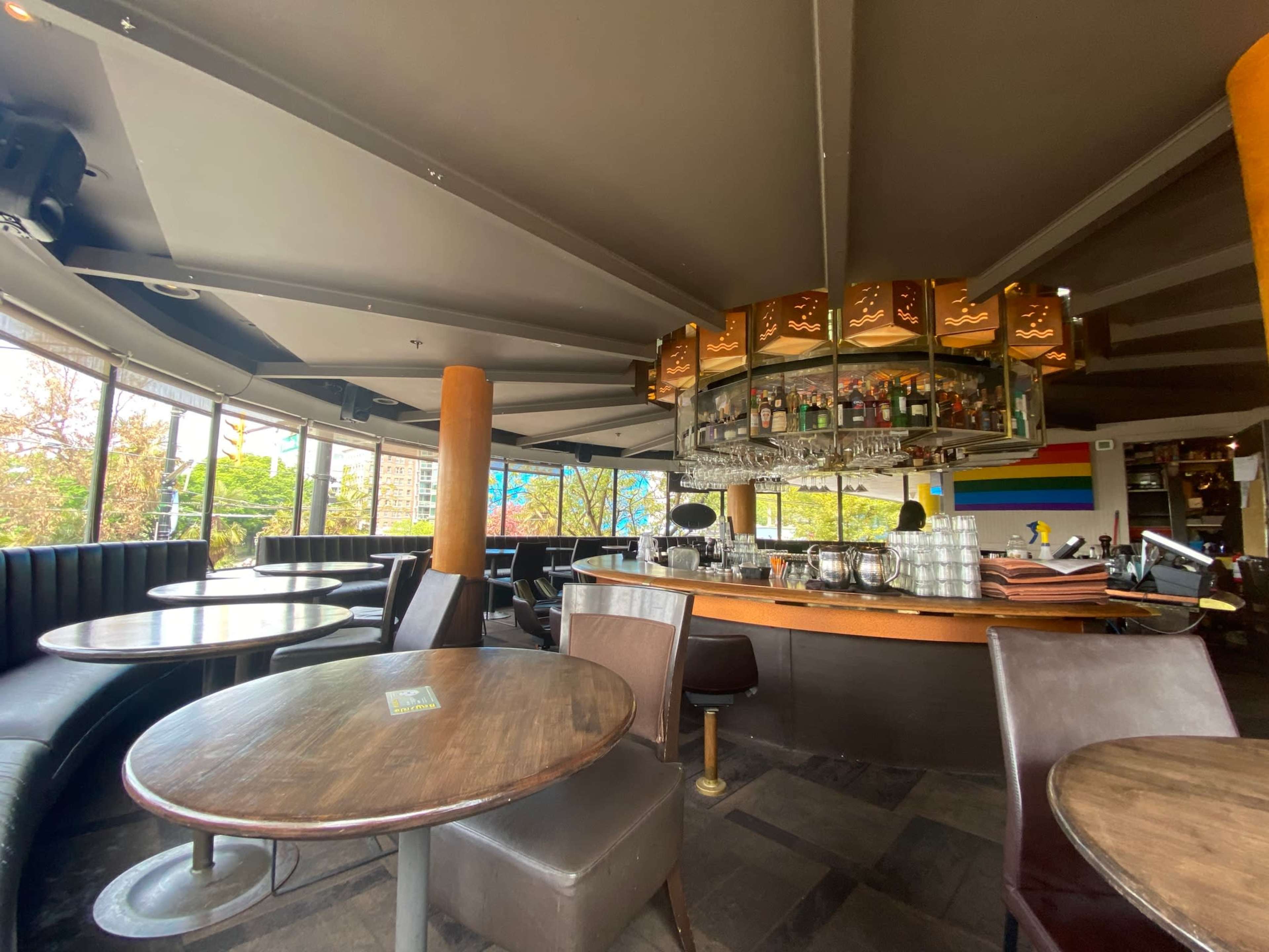 A modern bar area with circular tables and a large bar counter featuring a circular display of bottles under an ornate light fixture.
