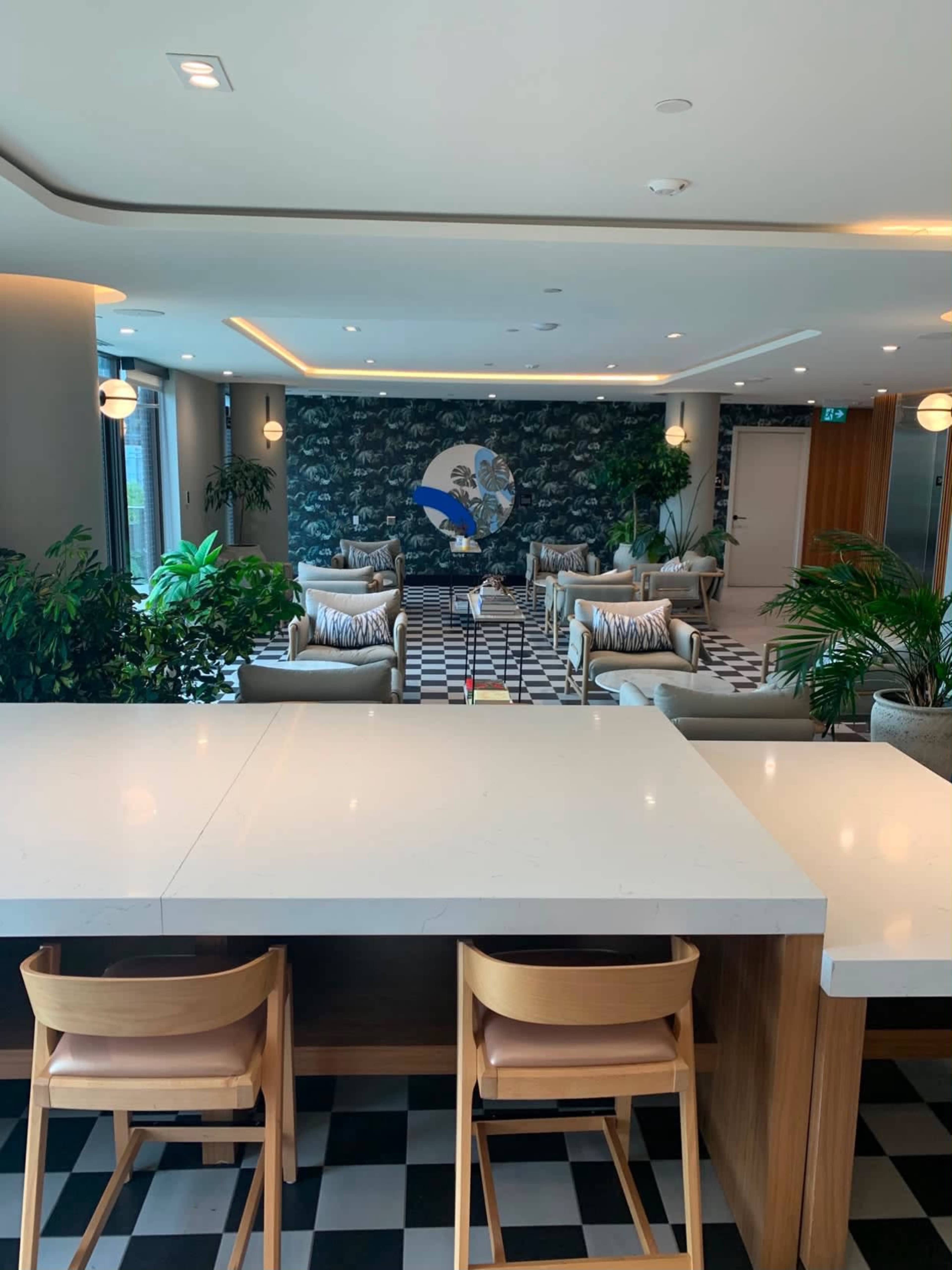 The image shows a modern lounge area with seating, plants, and a patterned wall in a well-lit interior space.