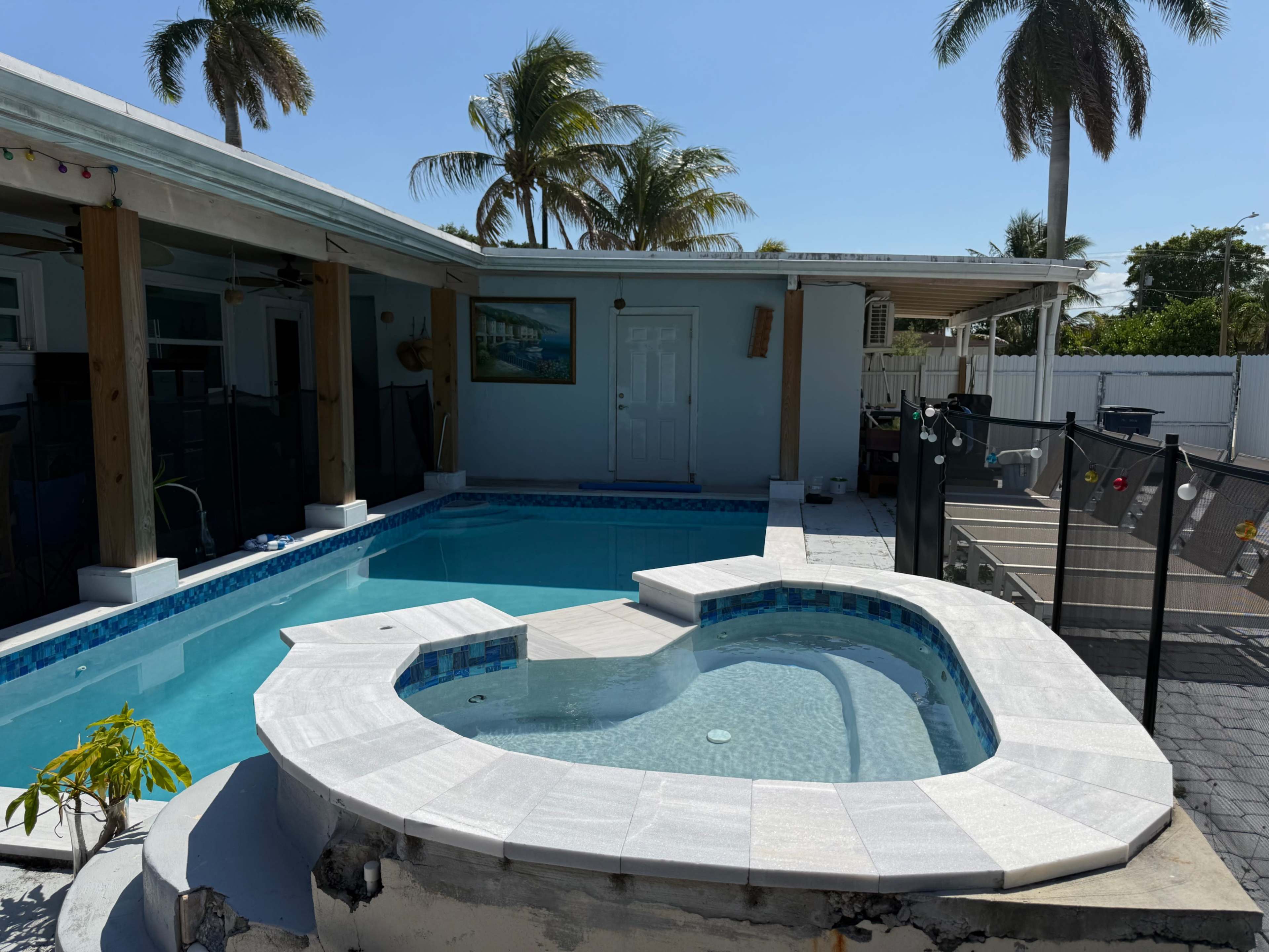 The image shows a swimming pool and spa area surrounded by palm trees and a patio.