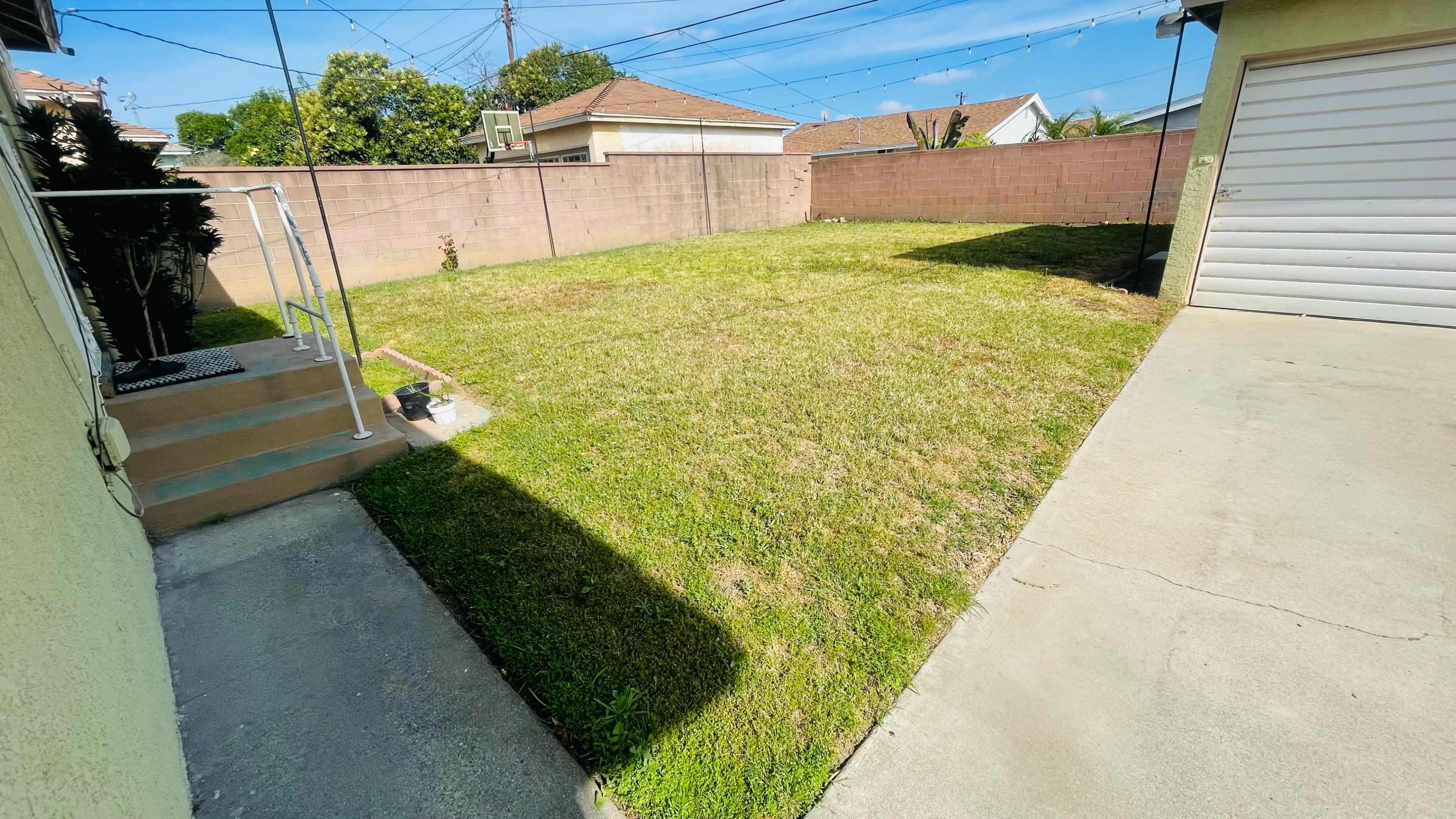 The image shows a grassy backyard with a concrete patio area and a fence surrounding the property.