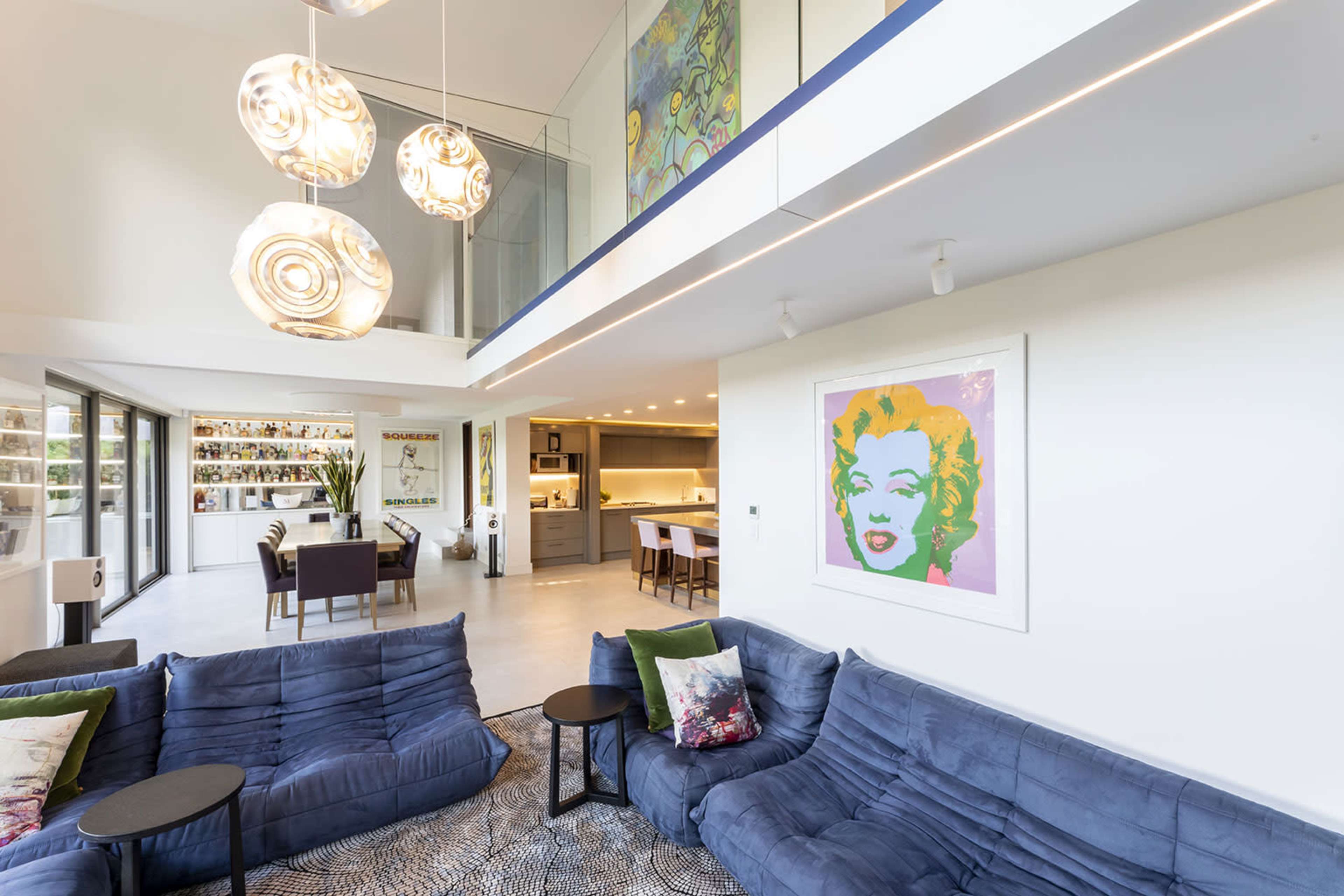 A stylish interior living space featuring blue sofas, modern lighting fixtures, a dining area, and a large artwork on the wall.