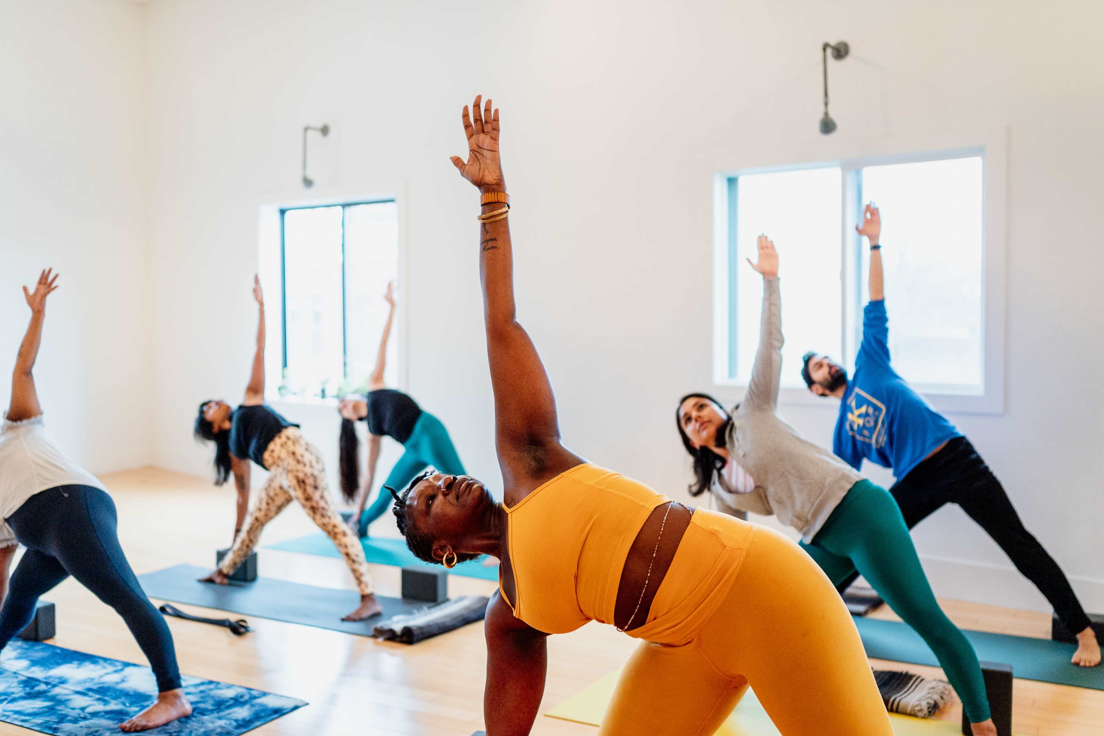 A group of people practices yoga in a brightly lit studio, each performing different poses.
