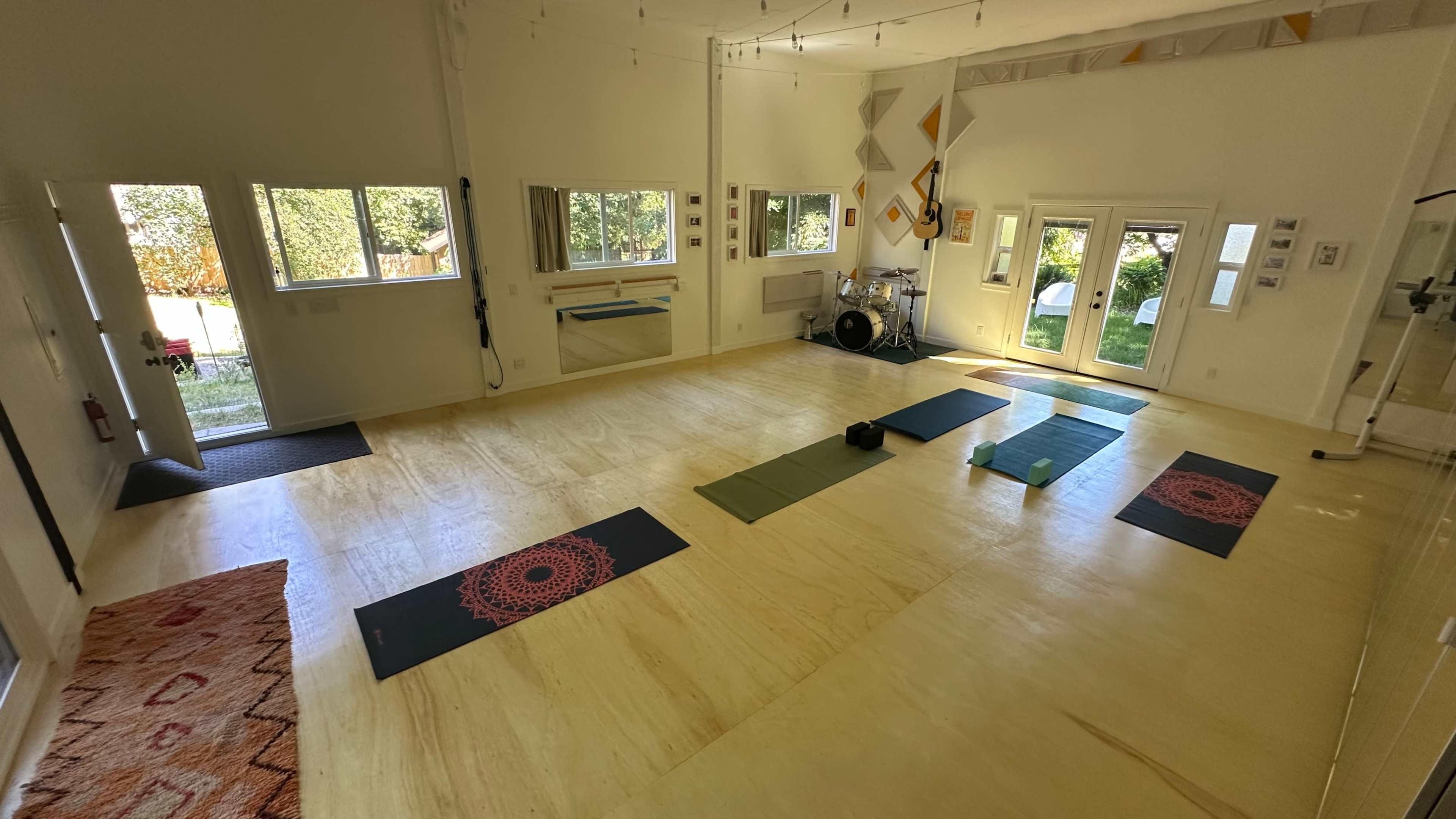 A spacious yoga studio features rolled out mats arranged neatly on a wooden floor, illuminated by natural light from large windows.