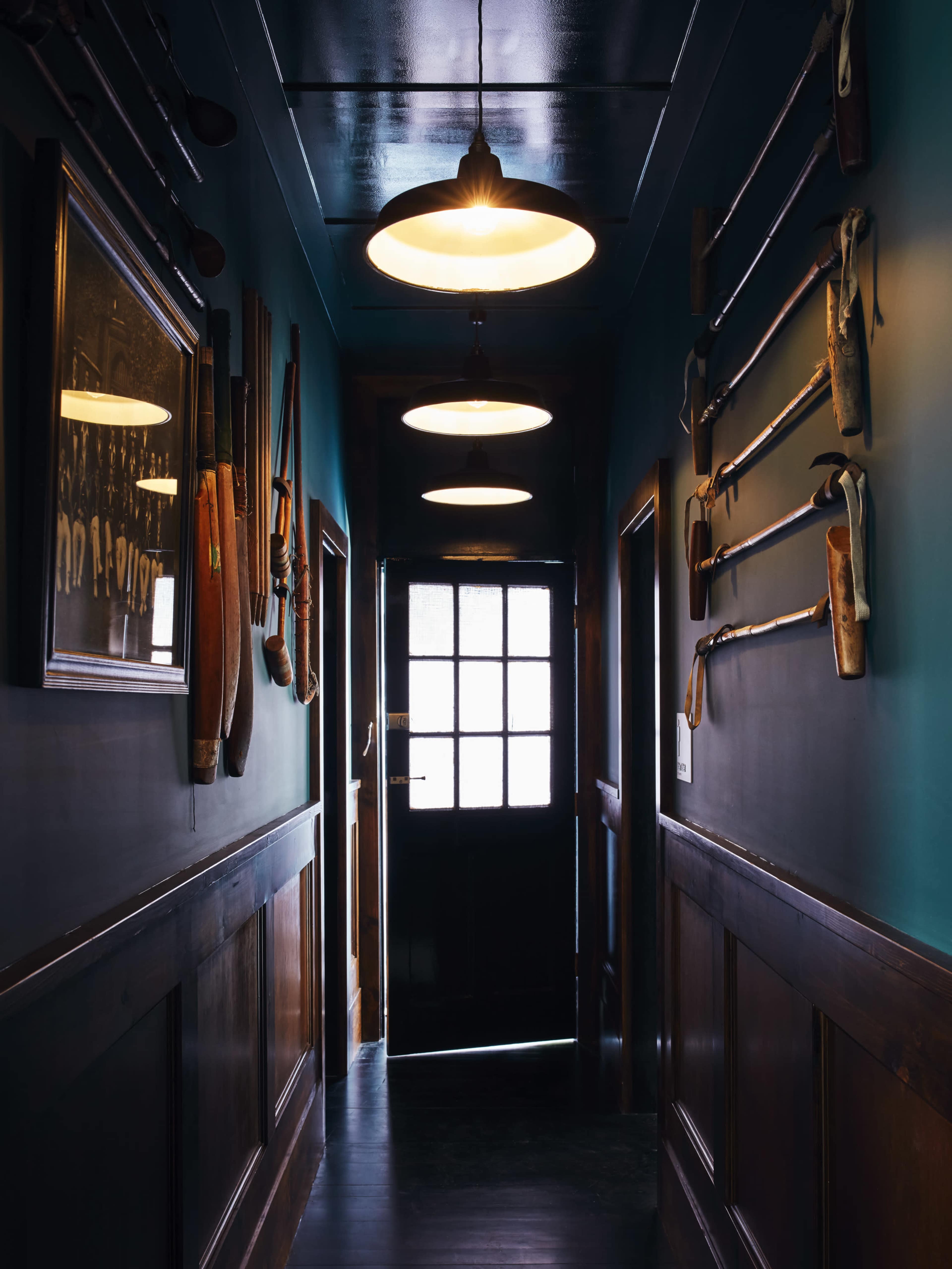 A narrow hallway features several illuminated pendant lights and walls adorned with various vintage tools and paddles.