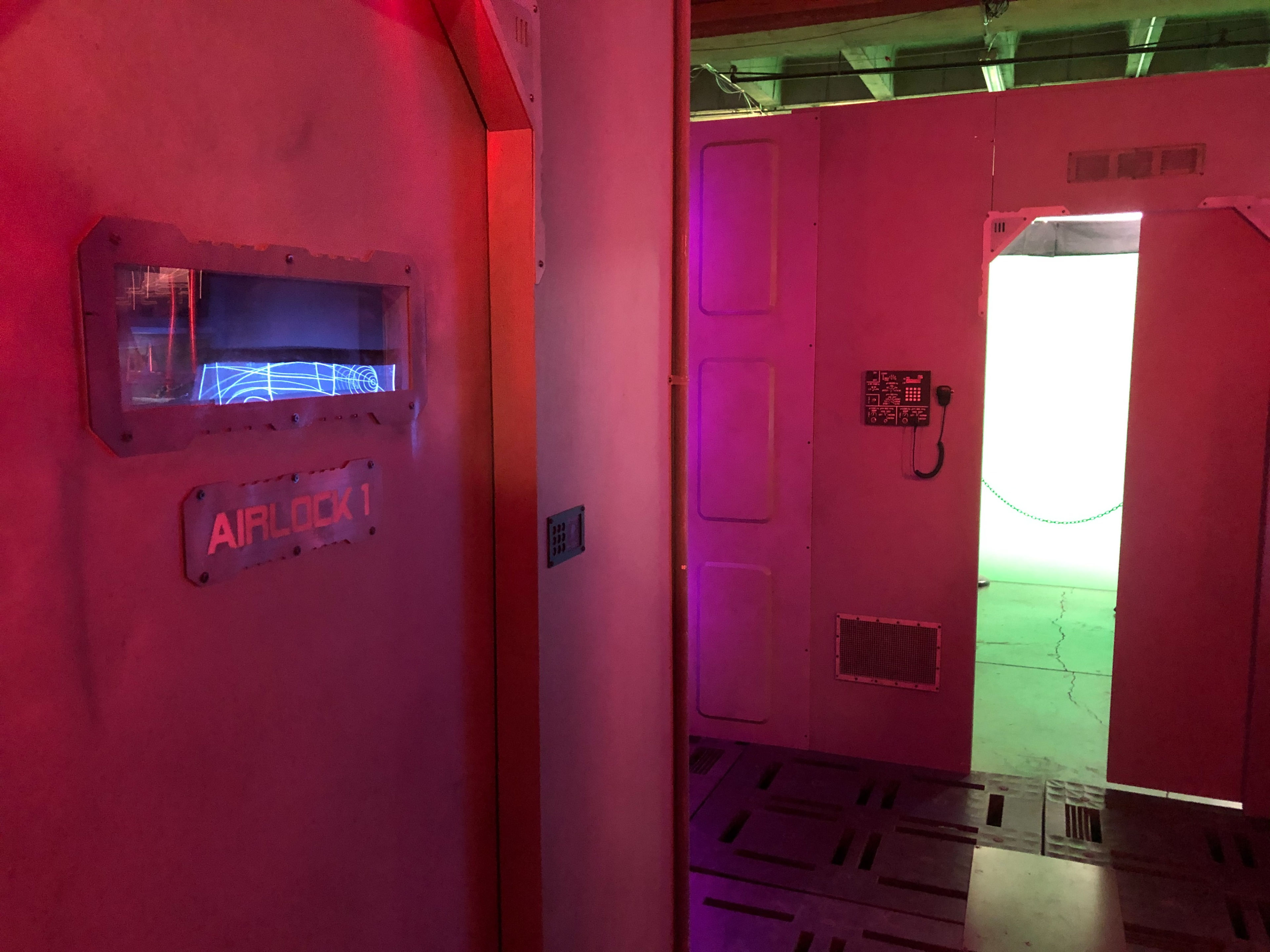 A corridor with a sign labeled "AIRLOCK 1" on a pink wall, leading to an adjacent door that has a green light illuminating the entrance.