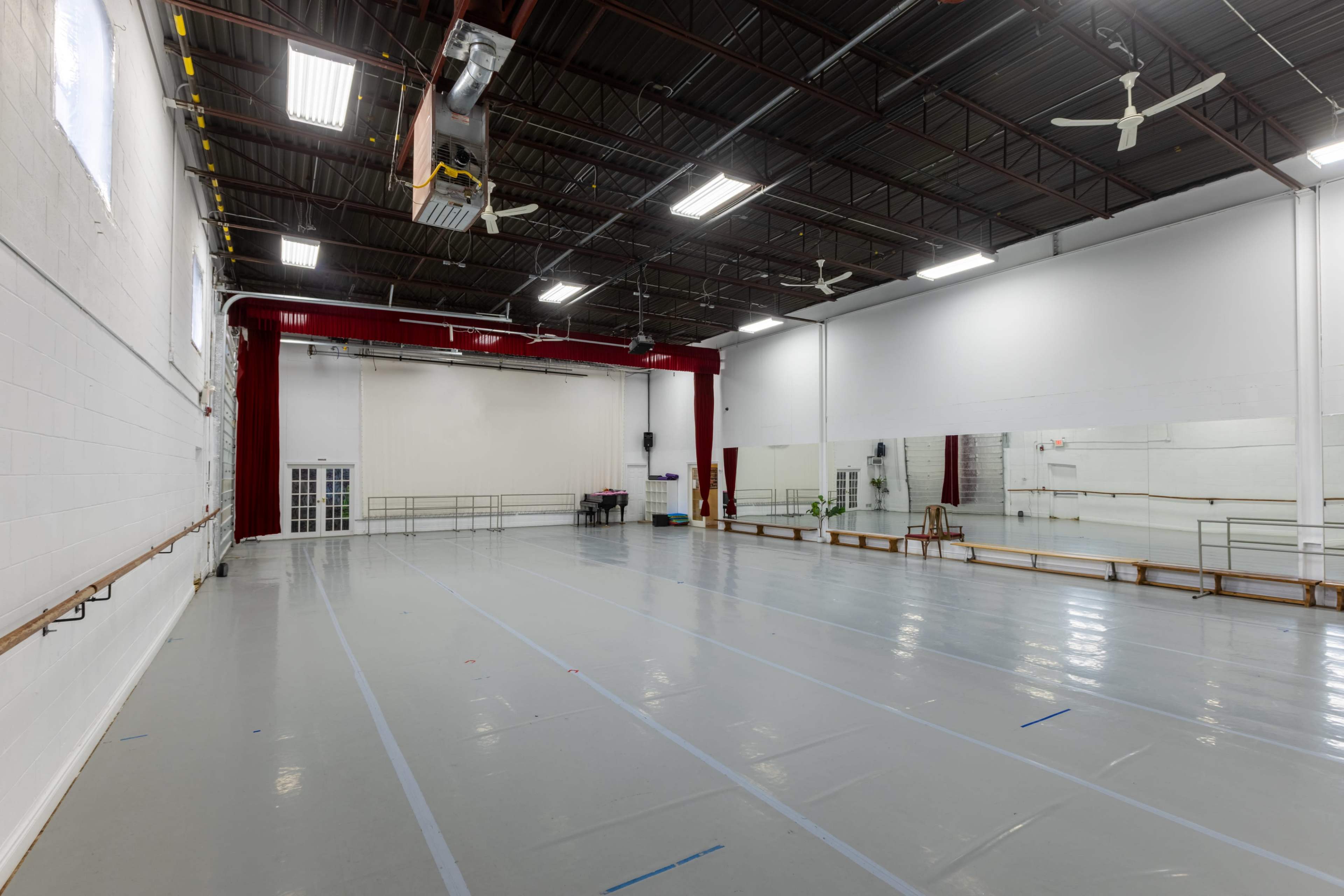 The image shows a spacious dance studio with a mirrored wall, wooden ballet barres, and a polished floor under bright overhead lights.