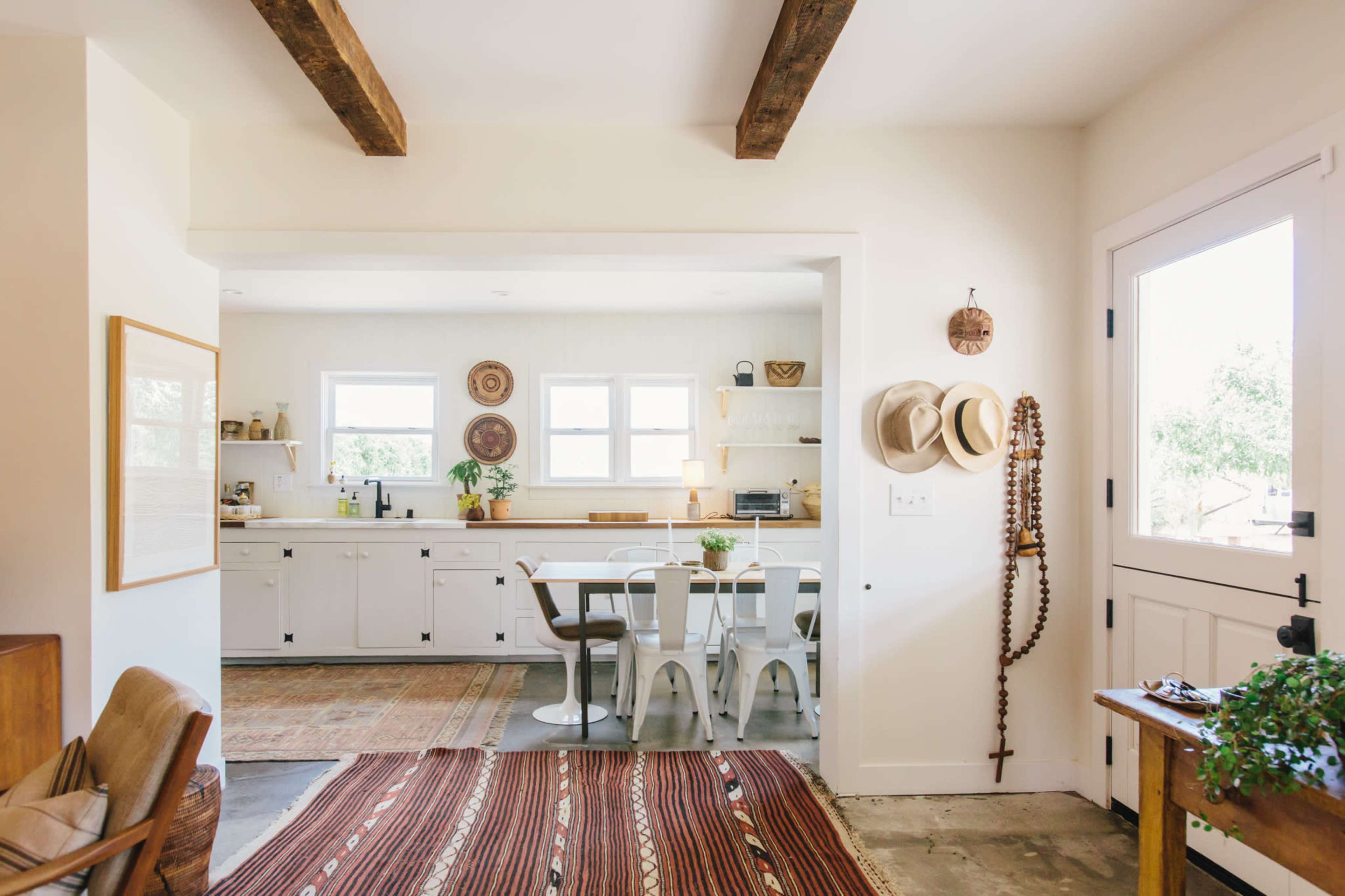 A bright, open-concept living area leads into a modern kitchen and dining space, featuring wooden beams and a mix of natural and decorative elements.
