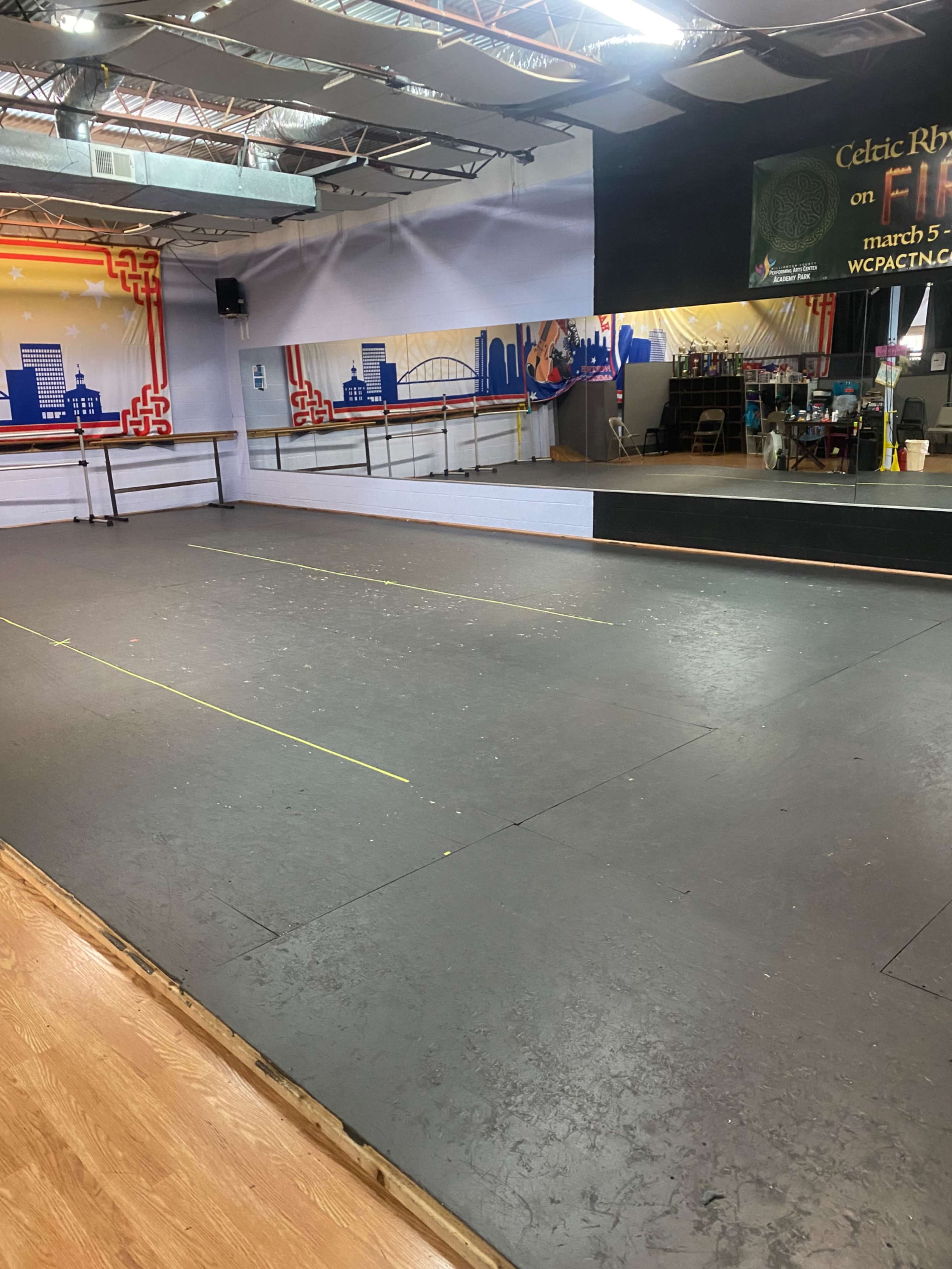 A dance studio with a mirrored wall, polished wooden floor, and marked floor spaces for practice.