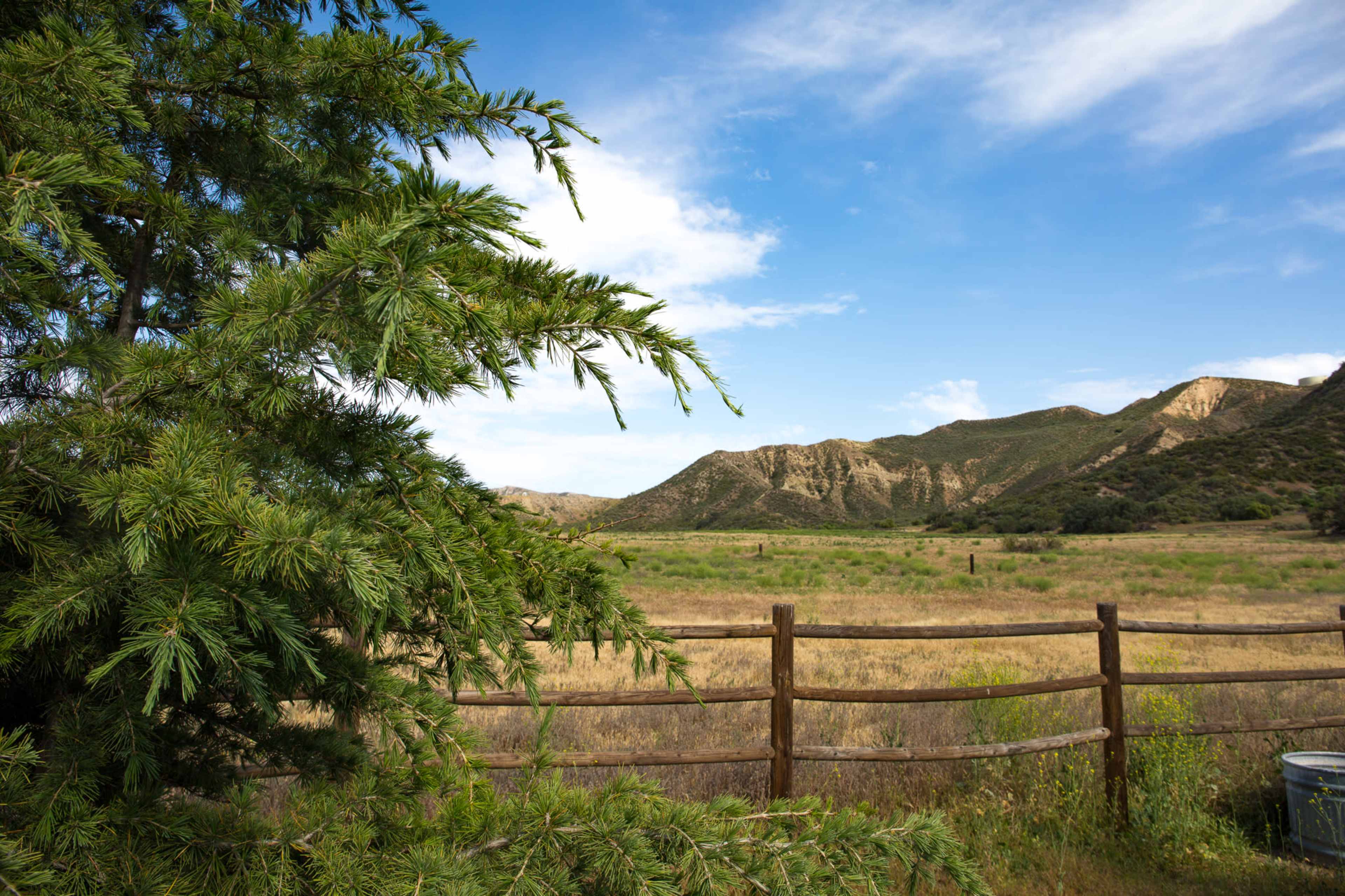 The image shows a landscape with a wooden fence, a grassy field, and distant mountains under a partly cloudy sky.
