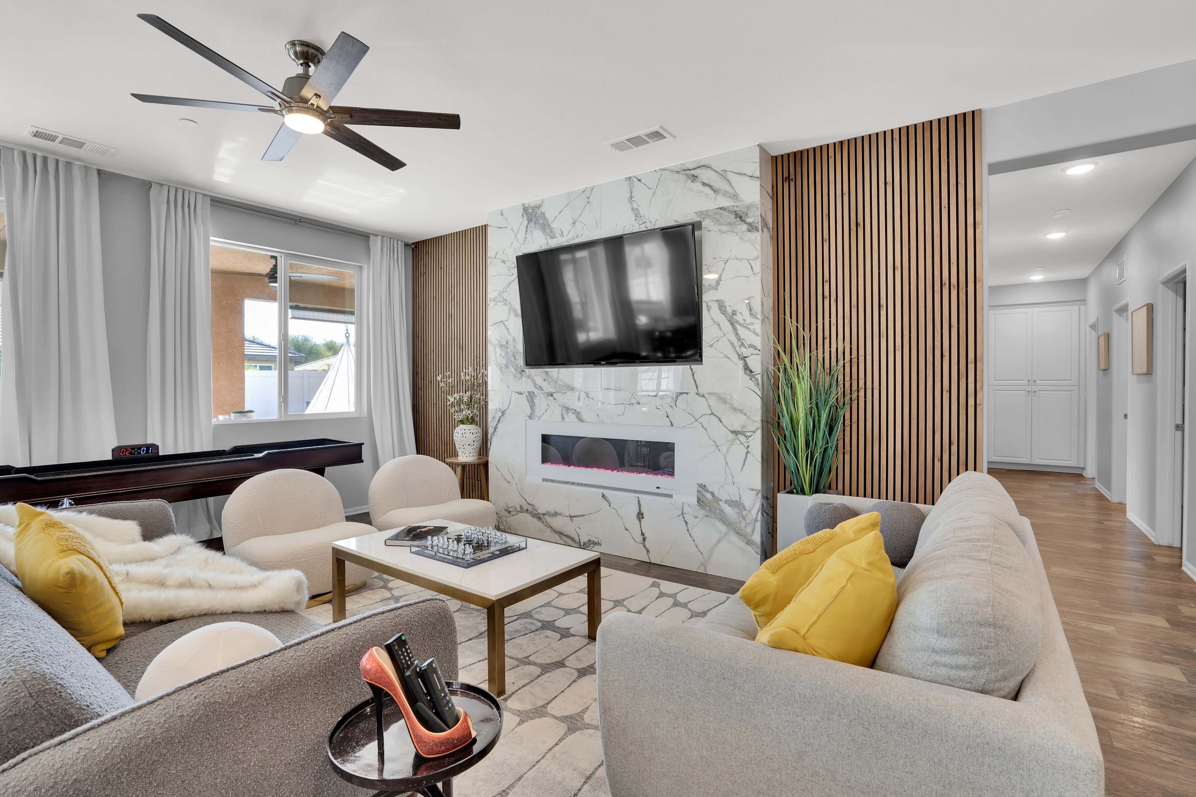 A modern living room with a marble fireplace, a wall-mounted television, and a light-colored seating arrangement.