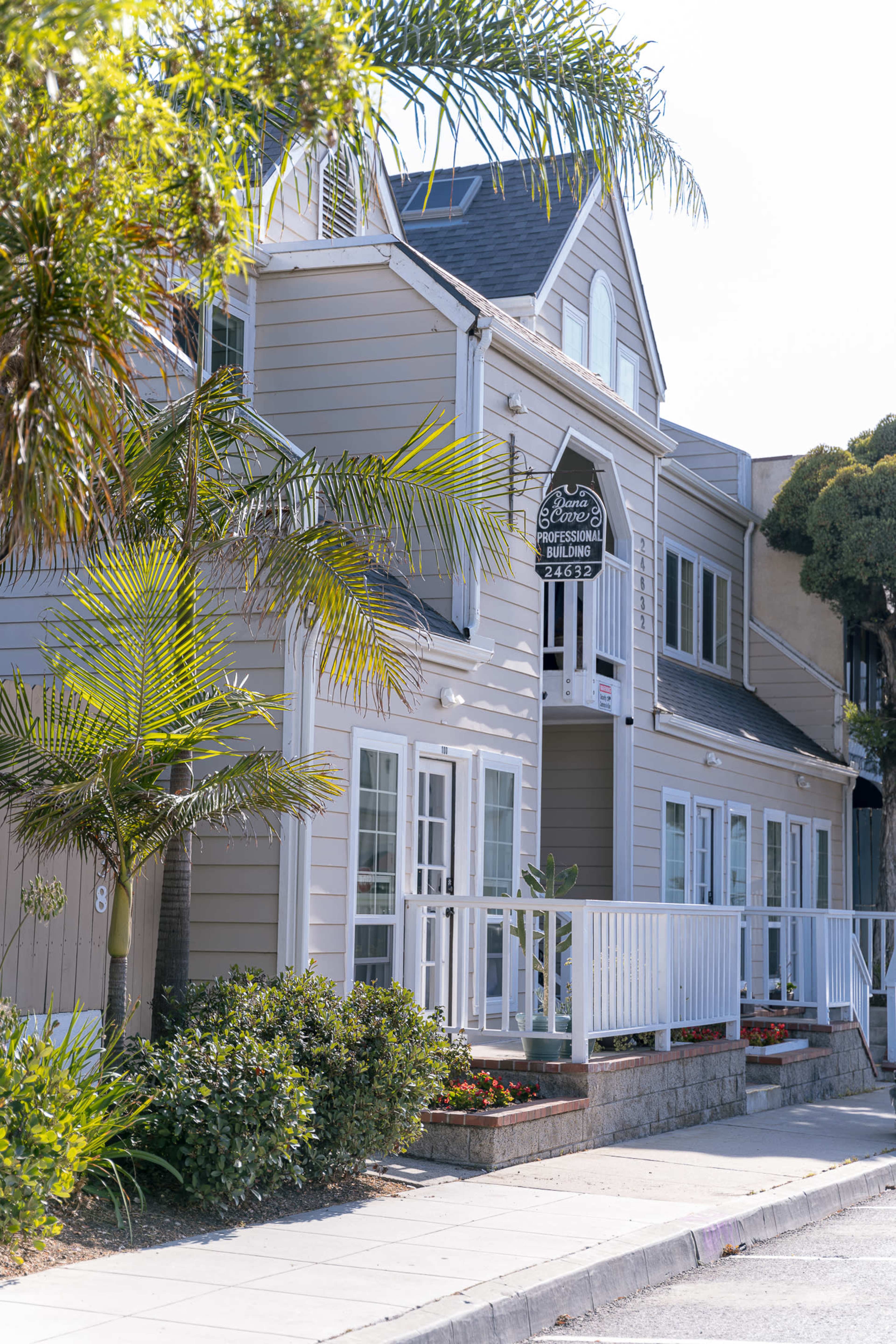 A two-story building with a sign reading "The Guest House" is flanked by palm trees and features a white railing along the front porch.