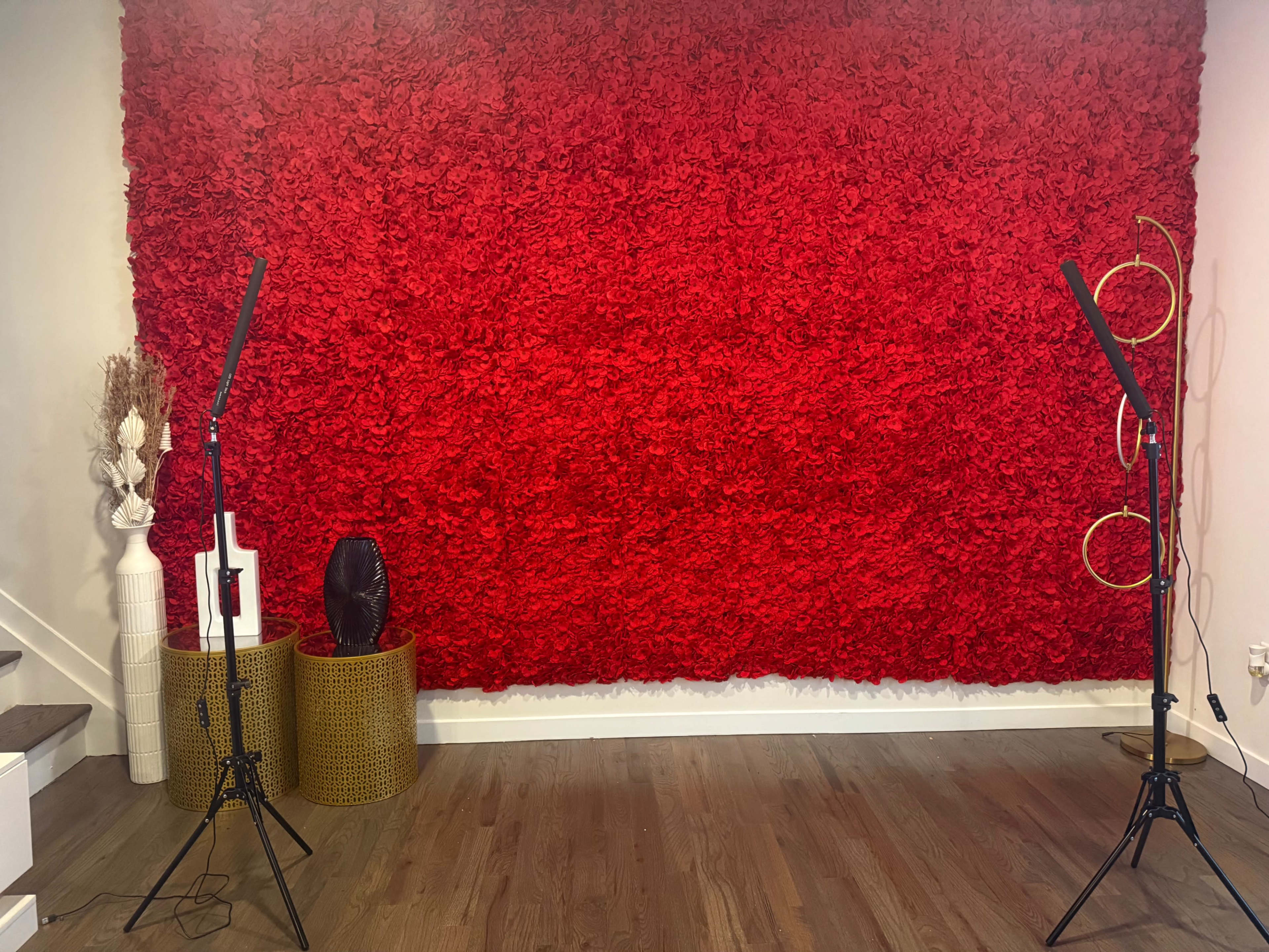 The image shows a room with a vibrant red floral wall, flanked by two lighting stands and decorated with various stylish objects.